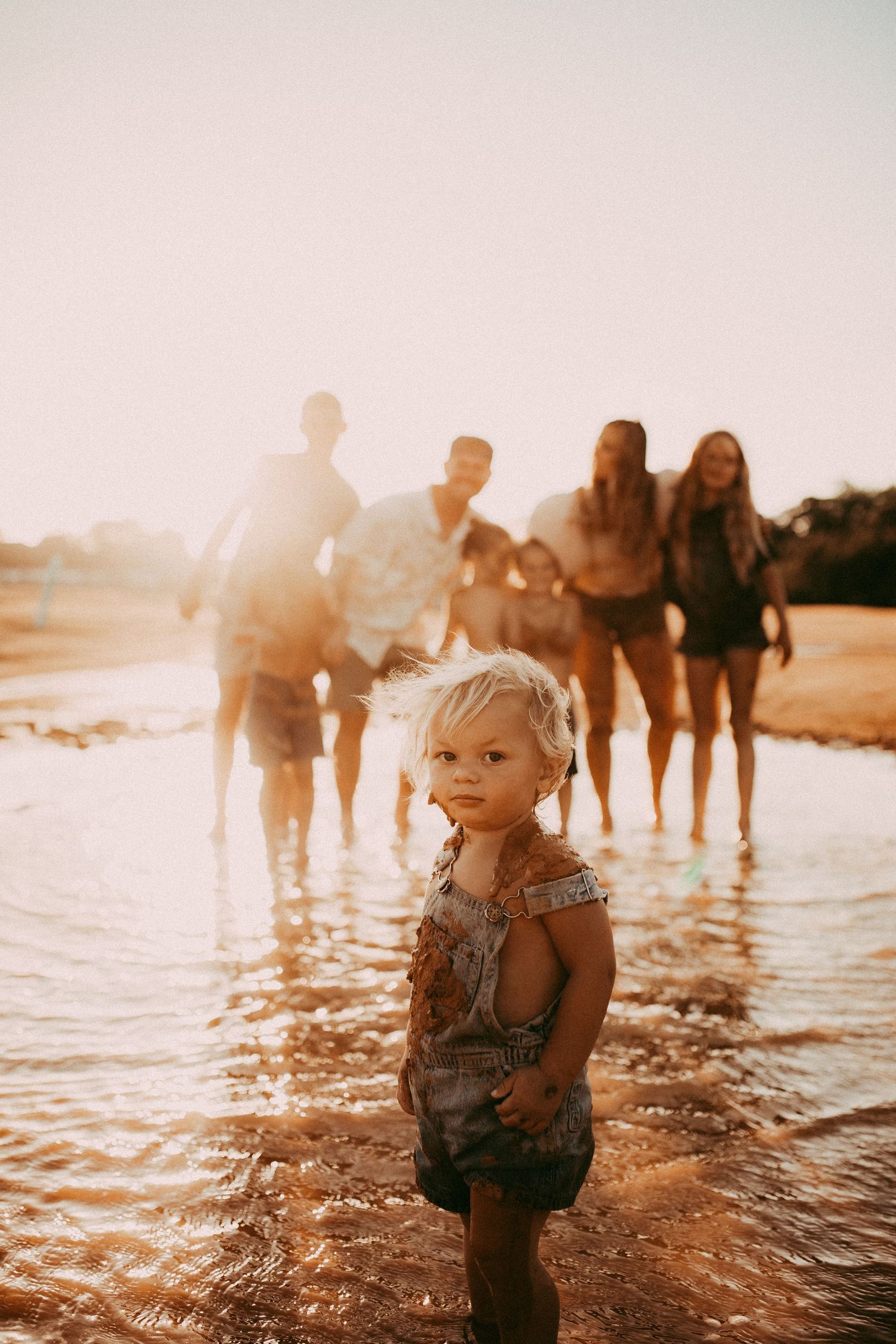 People enjoying a summer sunset at the beach while standing in shallow ocean water with warm golden sunshine.