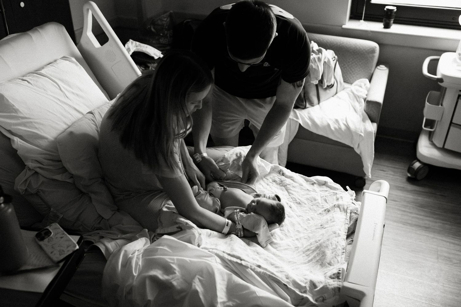 Black and white photo of parents in hospital room lovingly gazing at their newborn baby after birth.
