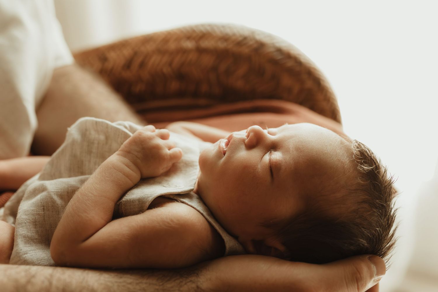 Peaceful newborn baby sleeping on a warm terracotta chair, wearing a soft linen outfit with tiny hands folded.