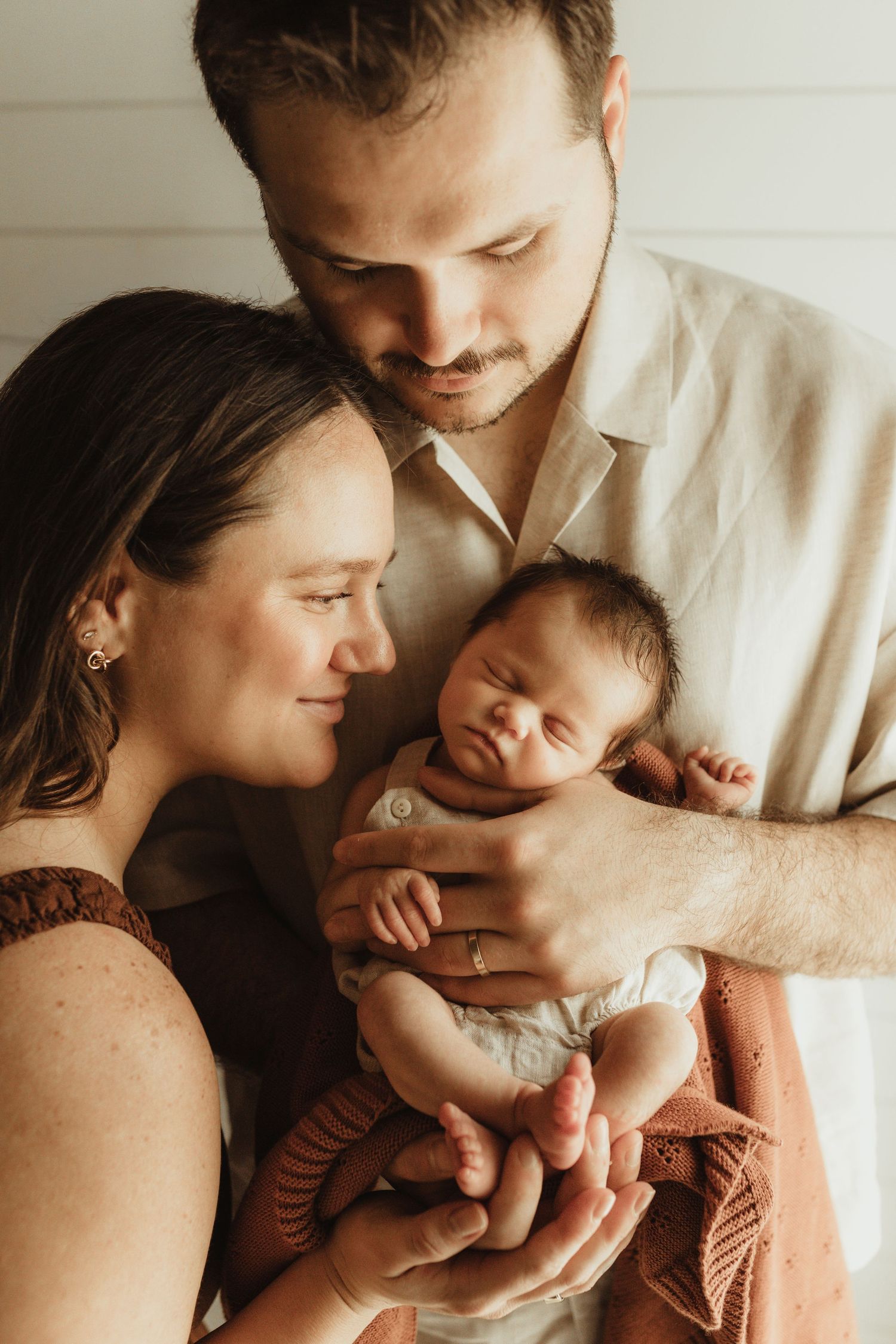 New parents tenderly cradling their sleeping newborn baby, sharing a precious family moment in warm, soft lighting.