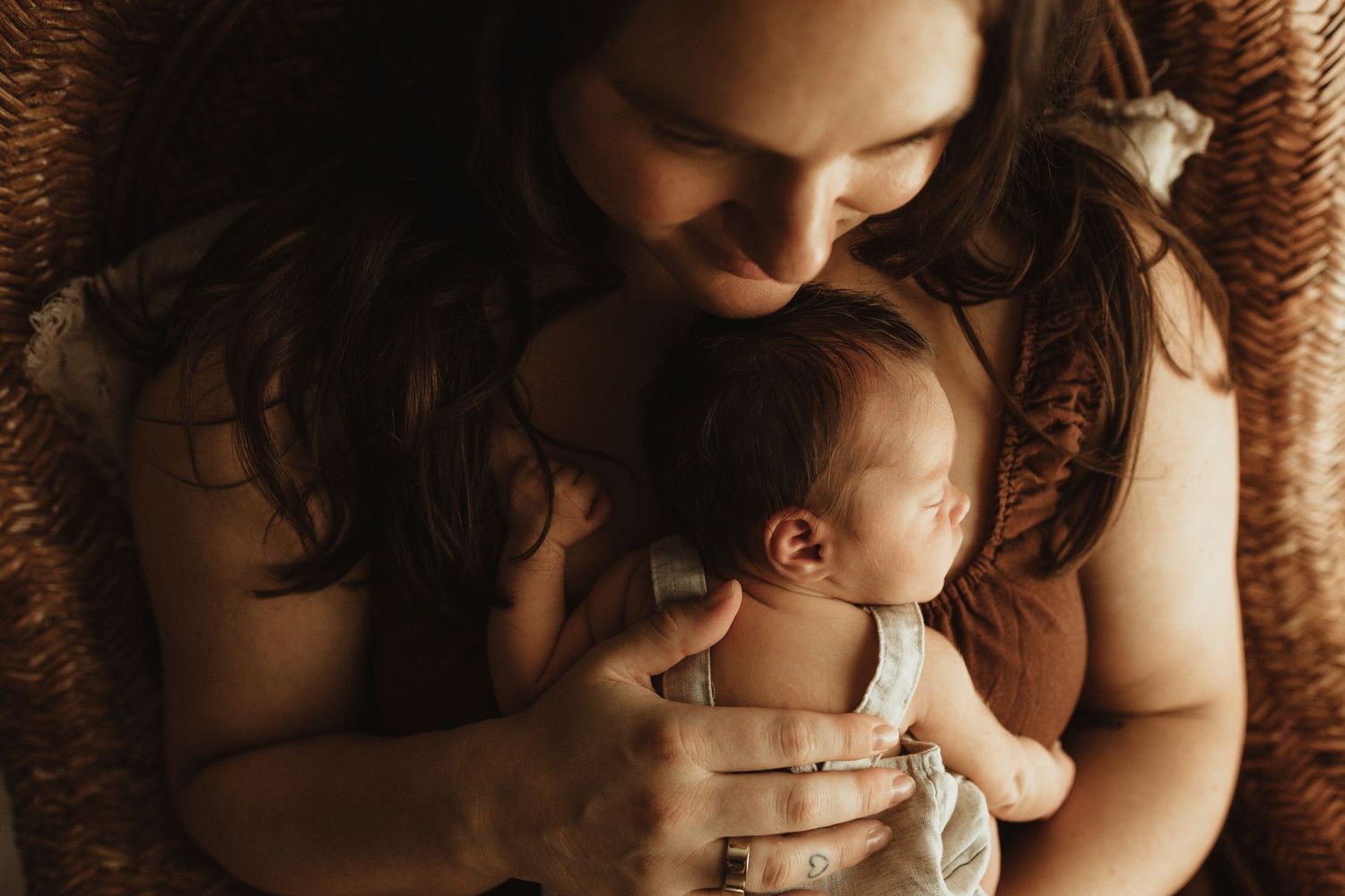 A mother tenderly holds her newborn baby close to her chest in a warm, intimate portrait photo.