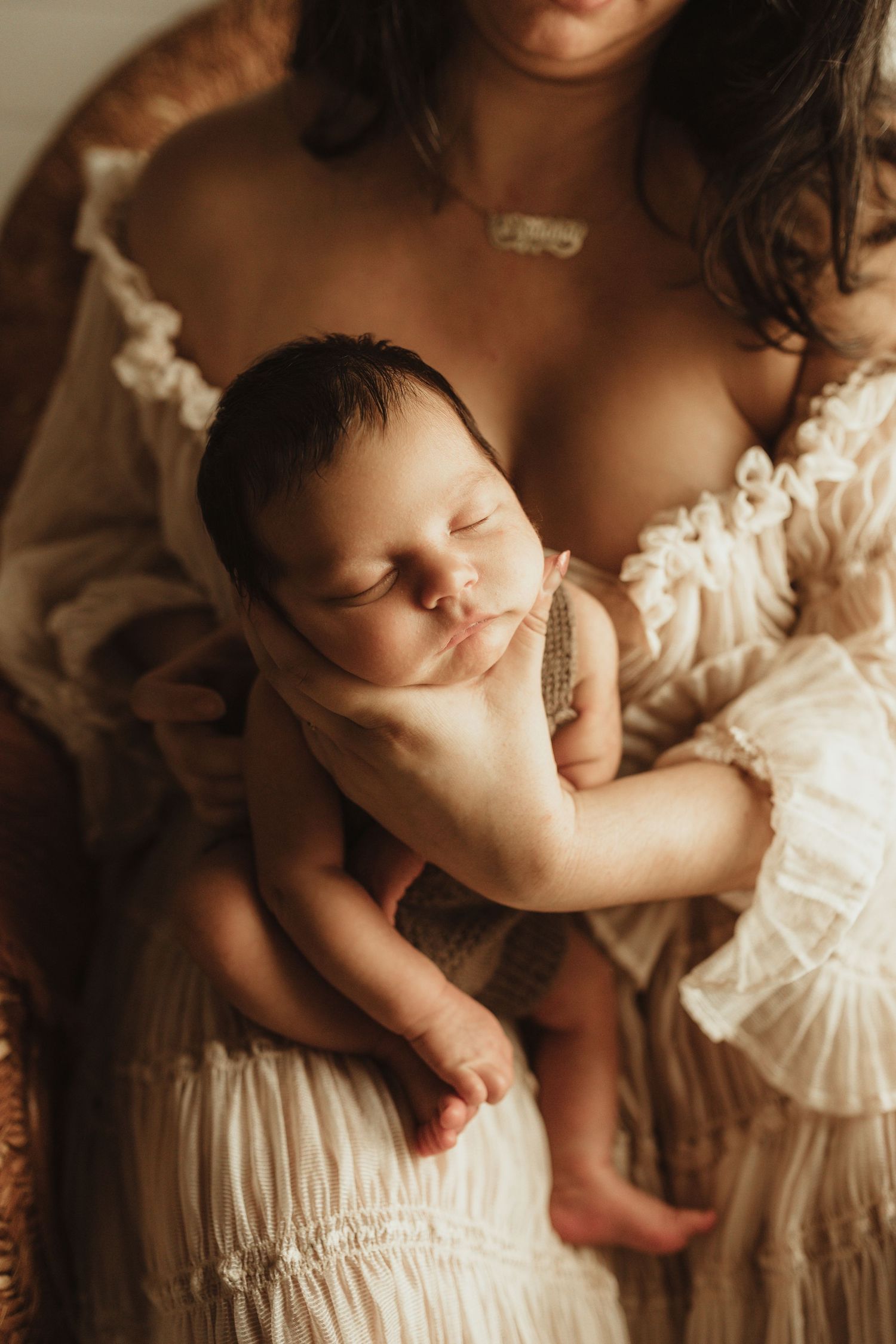 A sleeping newborn baby rests peacefully against soft white lace fabric in warm lighting.
