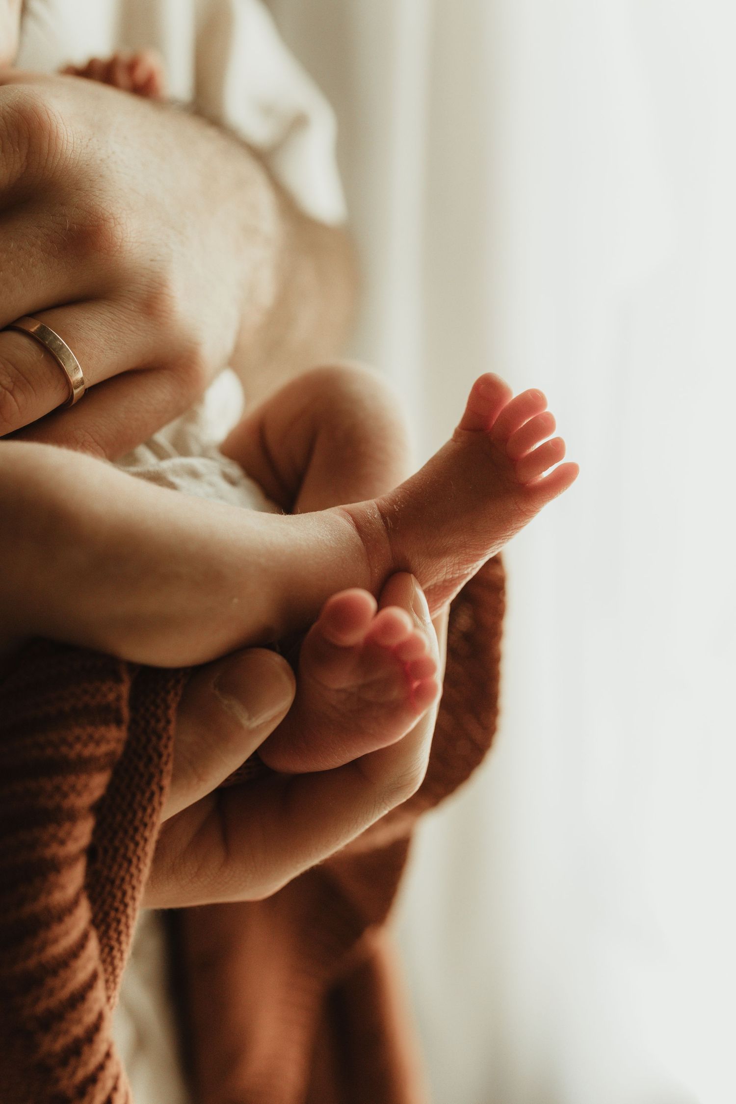 Close-up of a parent's hands gently holding tiny newborn baby feet wrapped in a warm knit blanket.