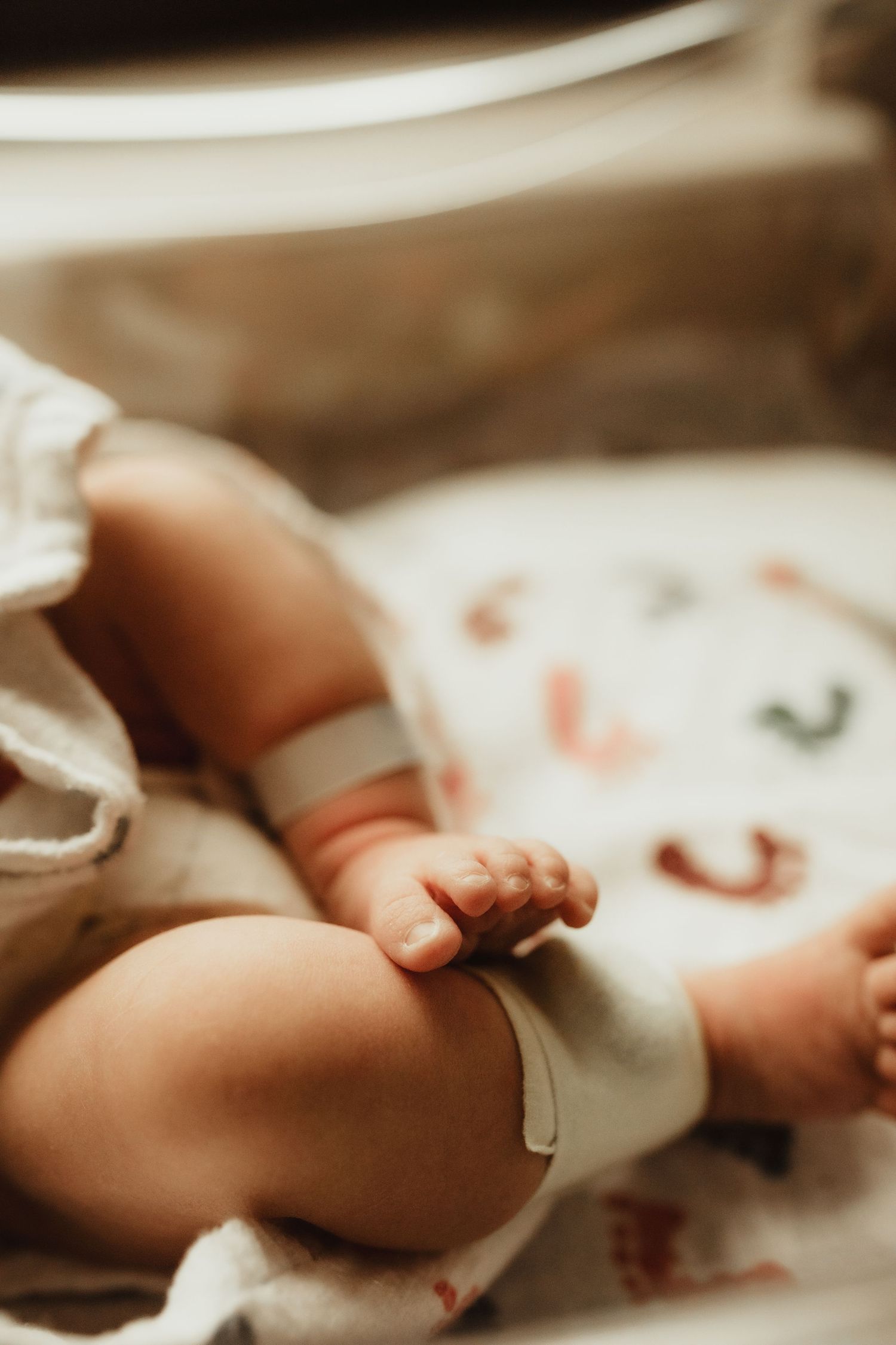 Close-up of a newborn baby's tiny hands and feet resting on a colorful patterned blanket in soft warm light.