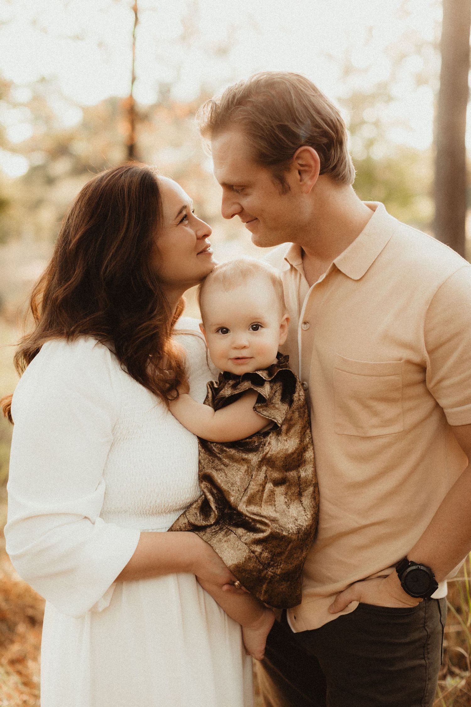 A tender family moment outdoors with a baby in a camo outfit surrounded by warm sunset light.