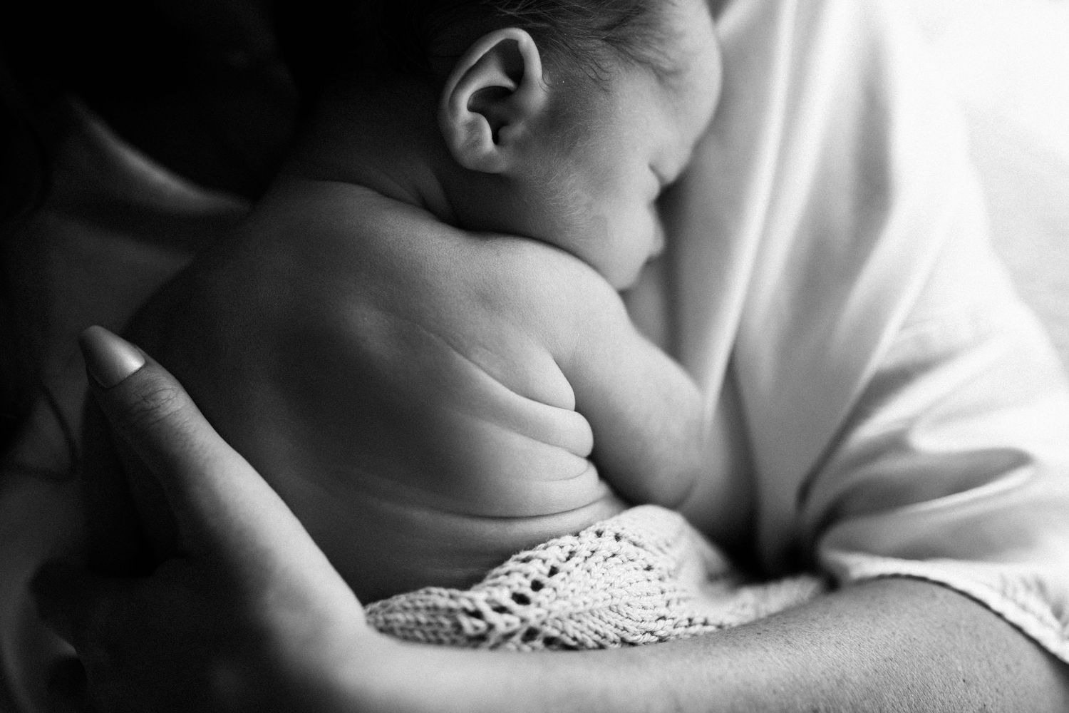 Black and white image of a baby wrapped in lace being held against white fabric.