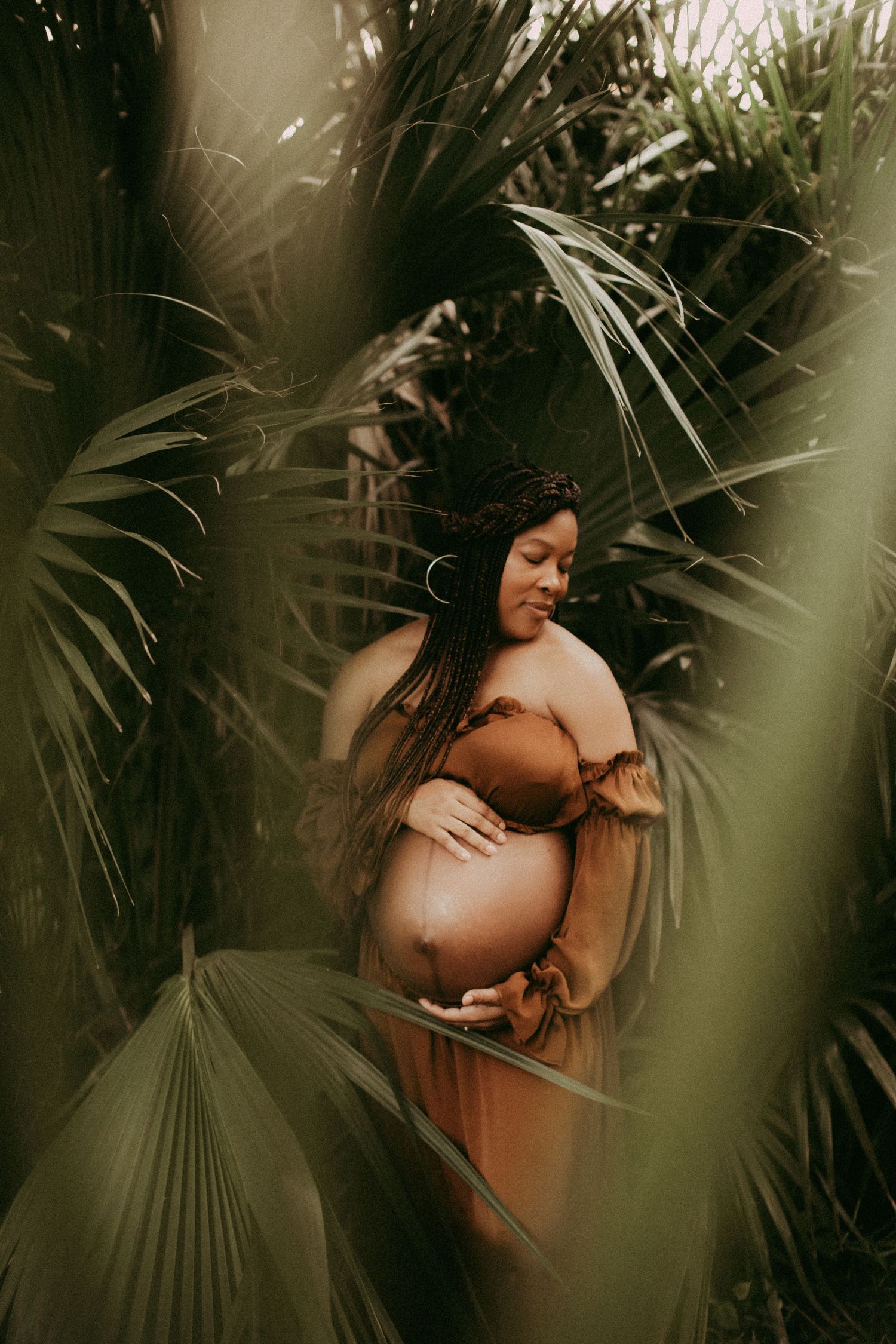 Artistic maternity photoshoot with tropical palm leaves and soft lighting creating a serene natural atmosphere.
