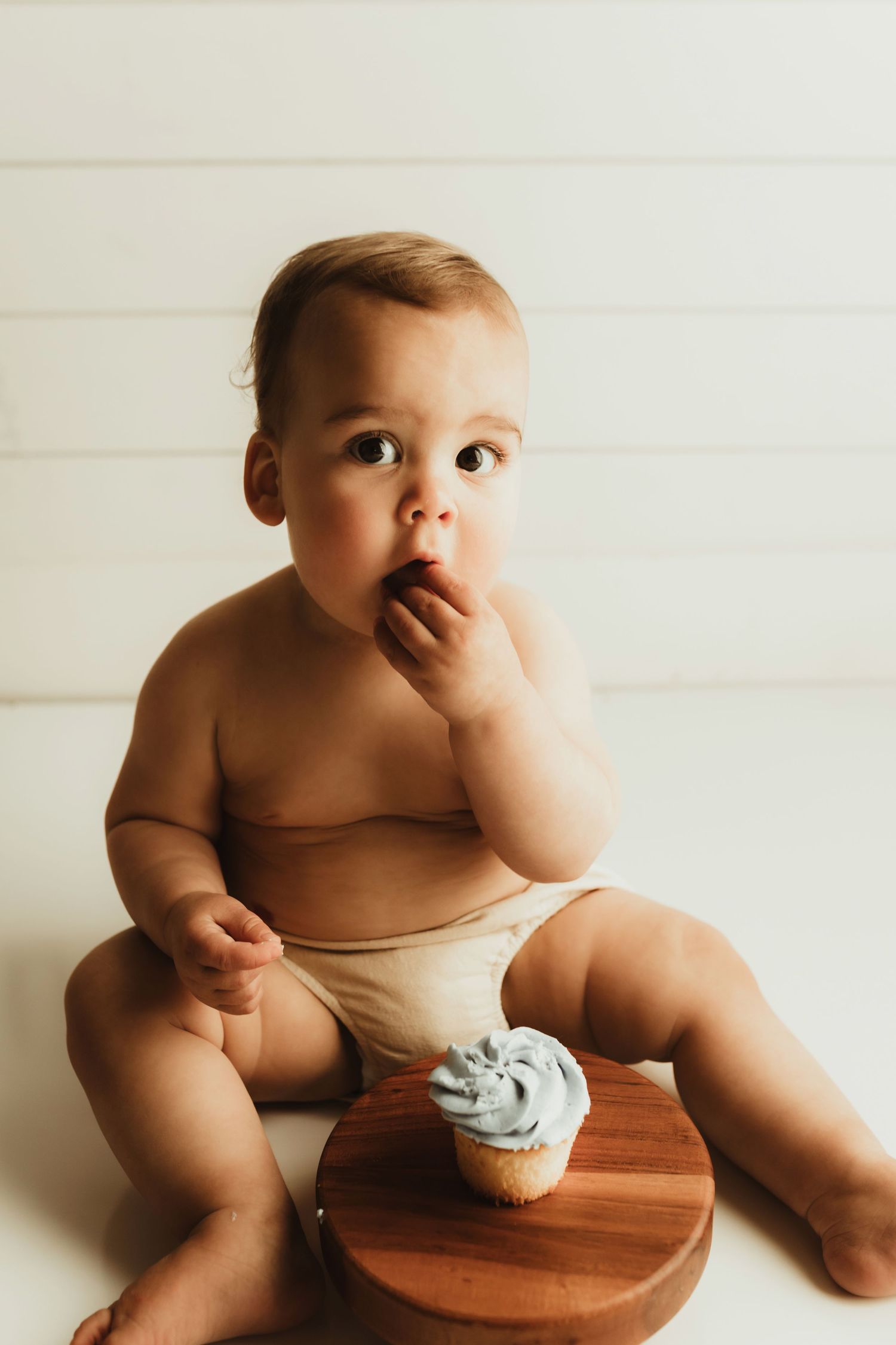 A baby in a white diaper sits on a wooden stool against a white background in a series of candid poses.