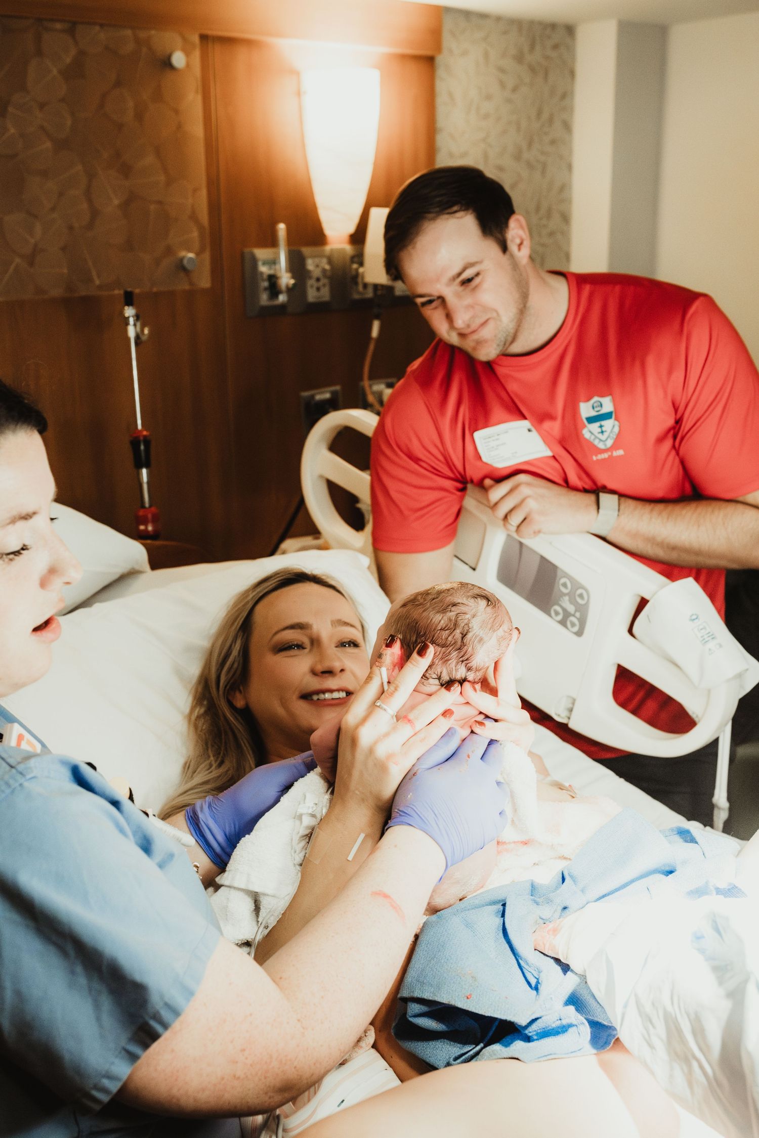 Healthcare provider in red scrubs performing a medical examination on a patient resting in a hospital bed.