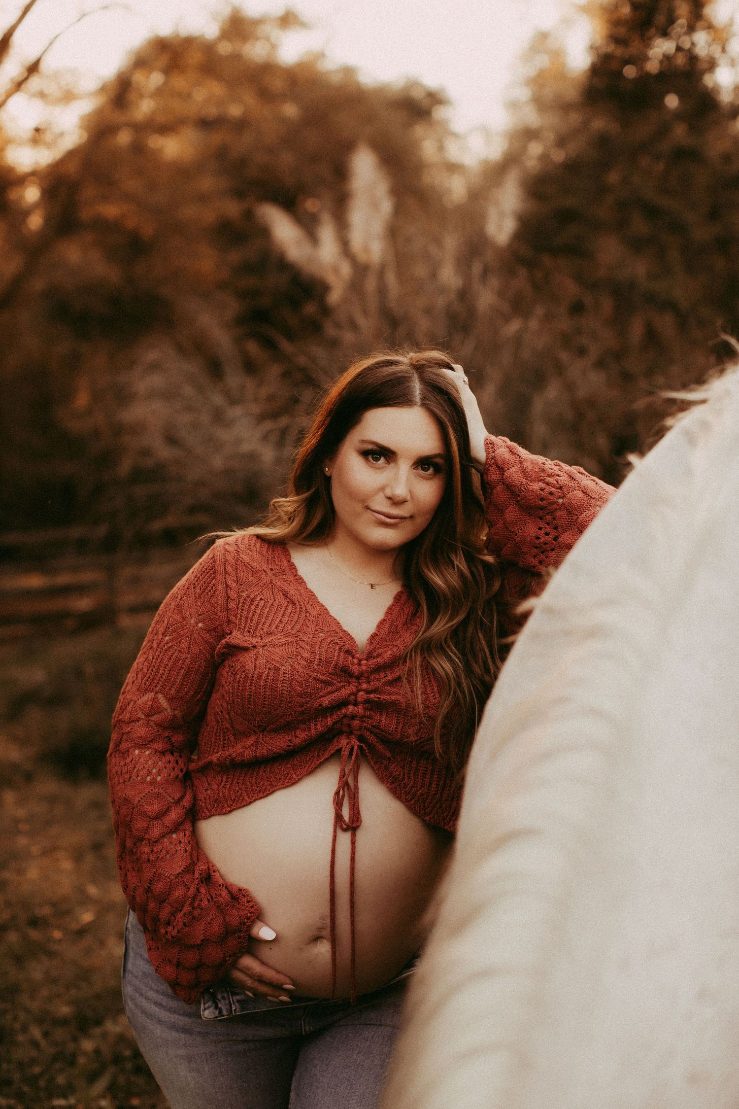 A series of maternity portraits in warm autumn tones showing a woman in a rustic red knit sweater outdoors.