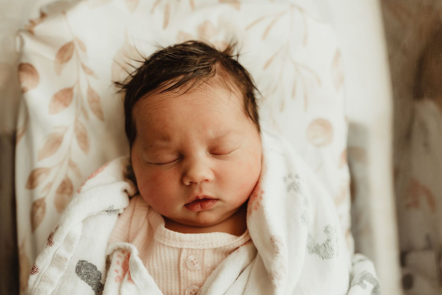 Peaceful sleeping newborn baby wrapped in white swaddle blanket against soft neutral background.