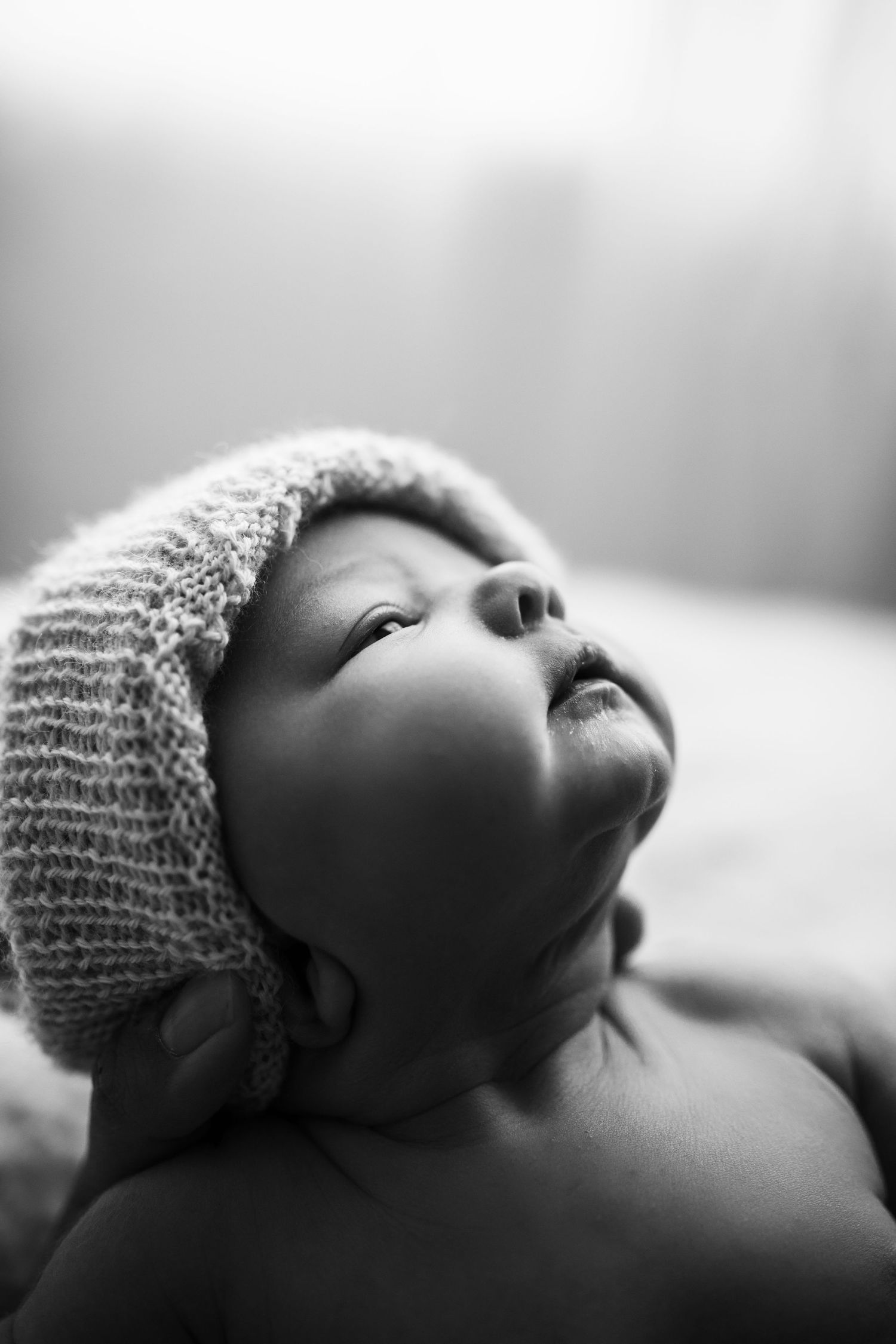 Black and white newborn portrait showing baby wearing knit cap against white backdrop.