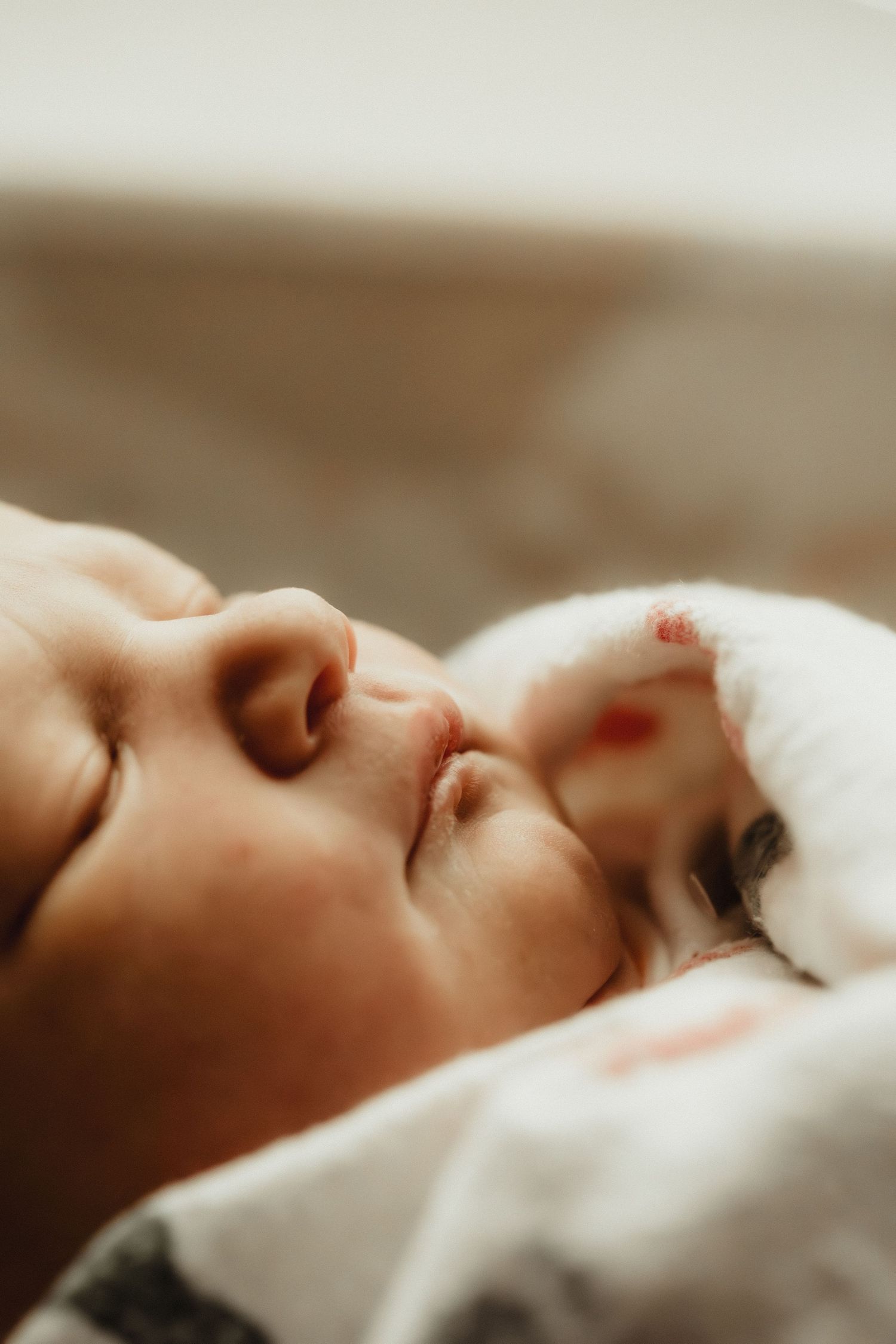Close-up of a peaceful sleeping newborn baby with tiny fist near face, wrapped in soft white blanket.