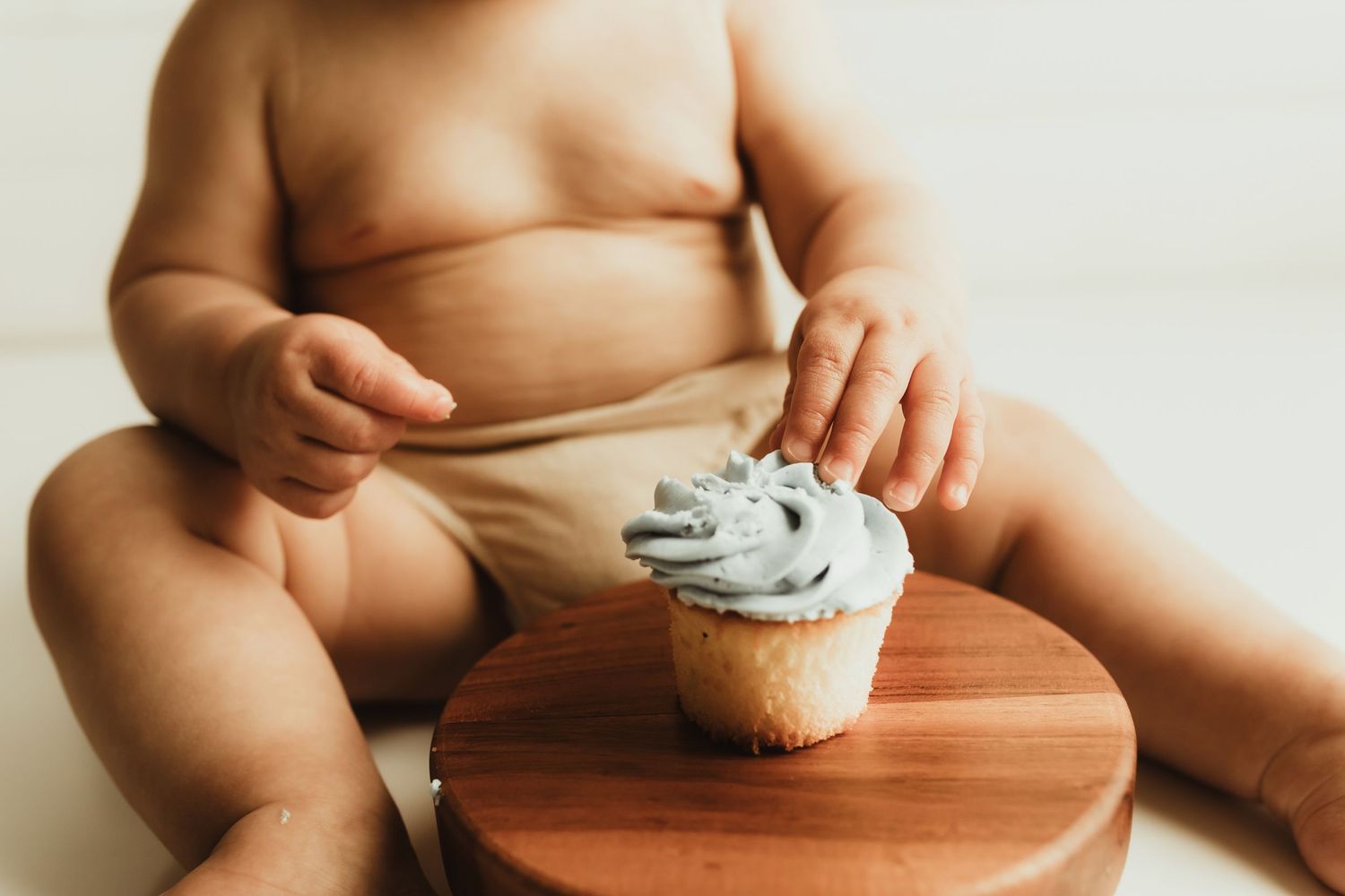 Baby's hands explore different food textures and items on a wooden surface during sensory play.