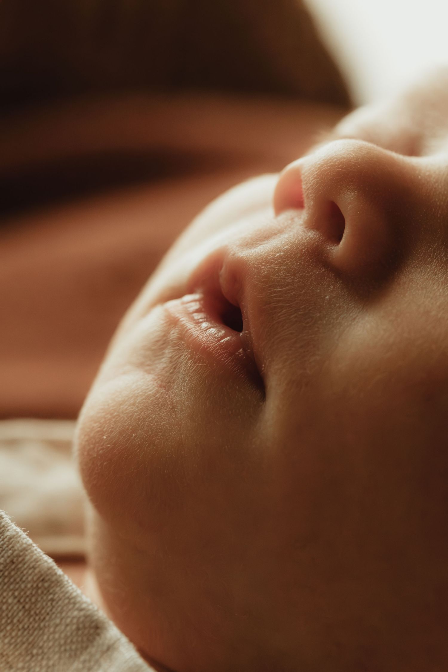 Close-up of a peaceful sleeping newborn baby's face with soft skin and tiny lips in warm light.