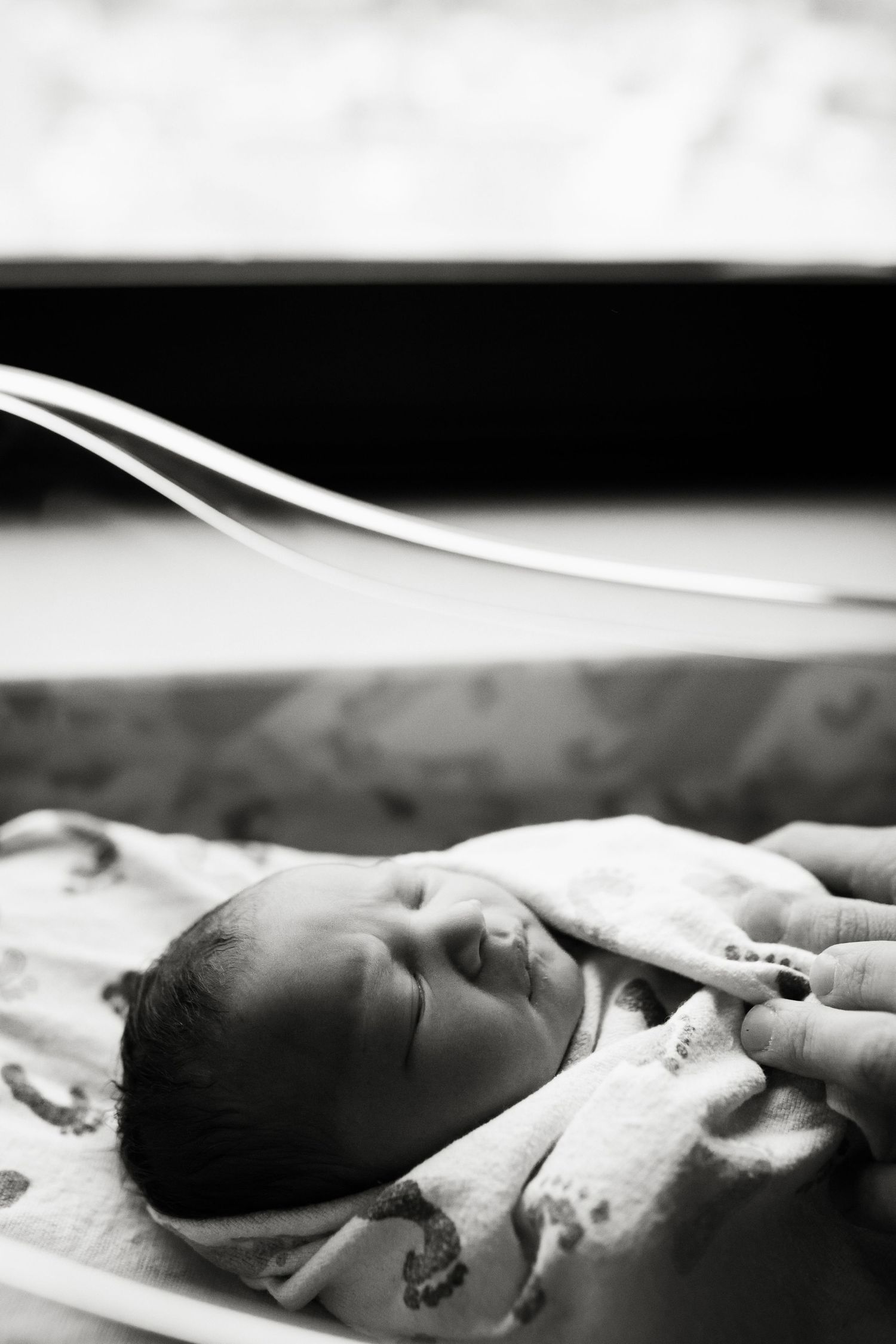 Black and white photo of a sleeping newborn baby wrapped in a blanket in a hospital bassinet.