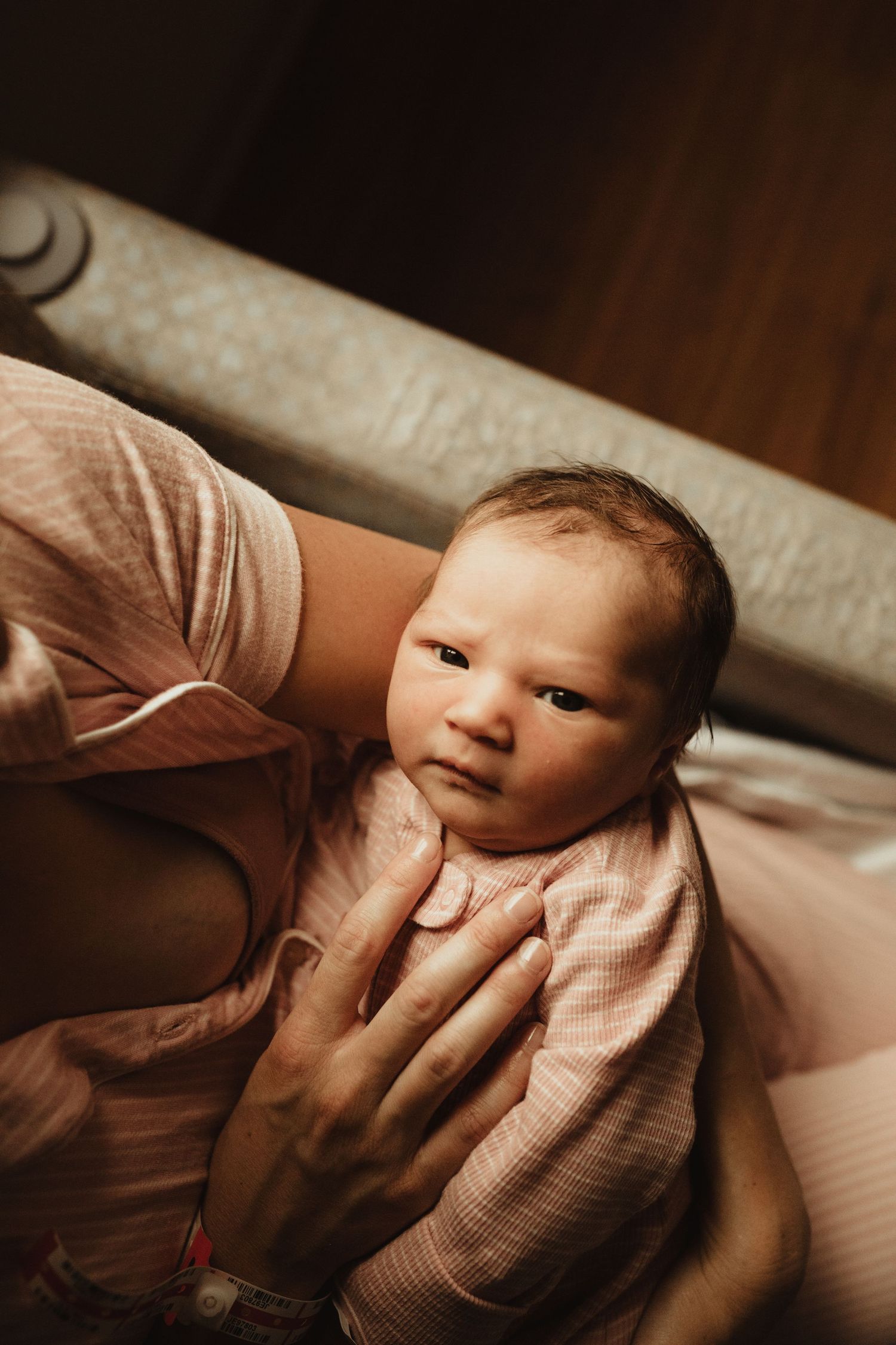 Newborn baby in pink outfit cradled in parent's arms, captured in warm, soft lighting.