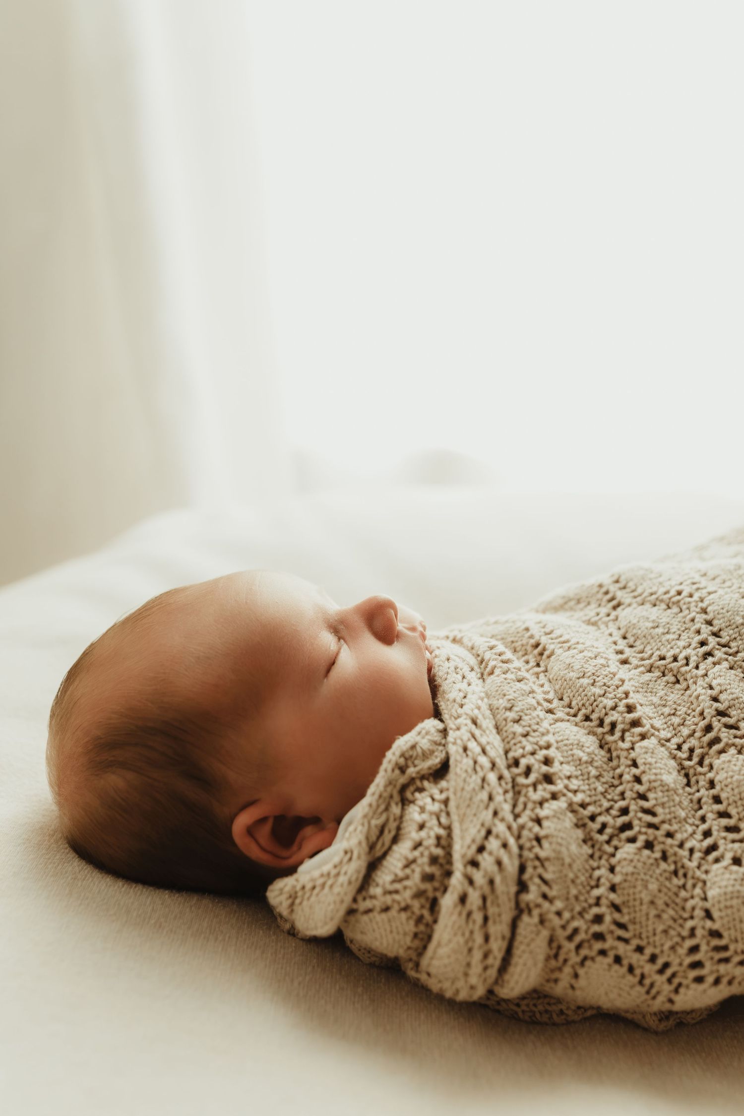 Peaceful newborn baby swaddled in a soft knit blanket, sleeping serenely on a white surface.