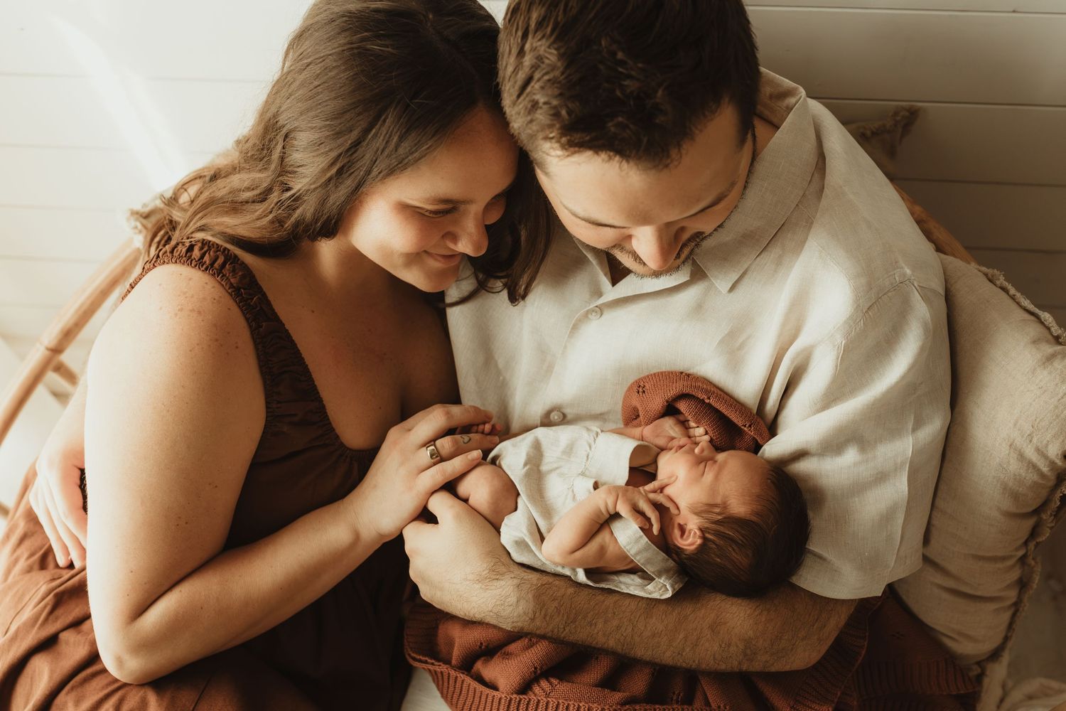 New parents lovingly gaze at their sleeping newborn baby during a warm, intimate family portrait session.