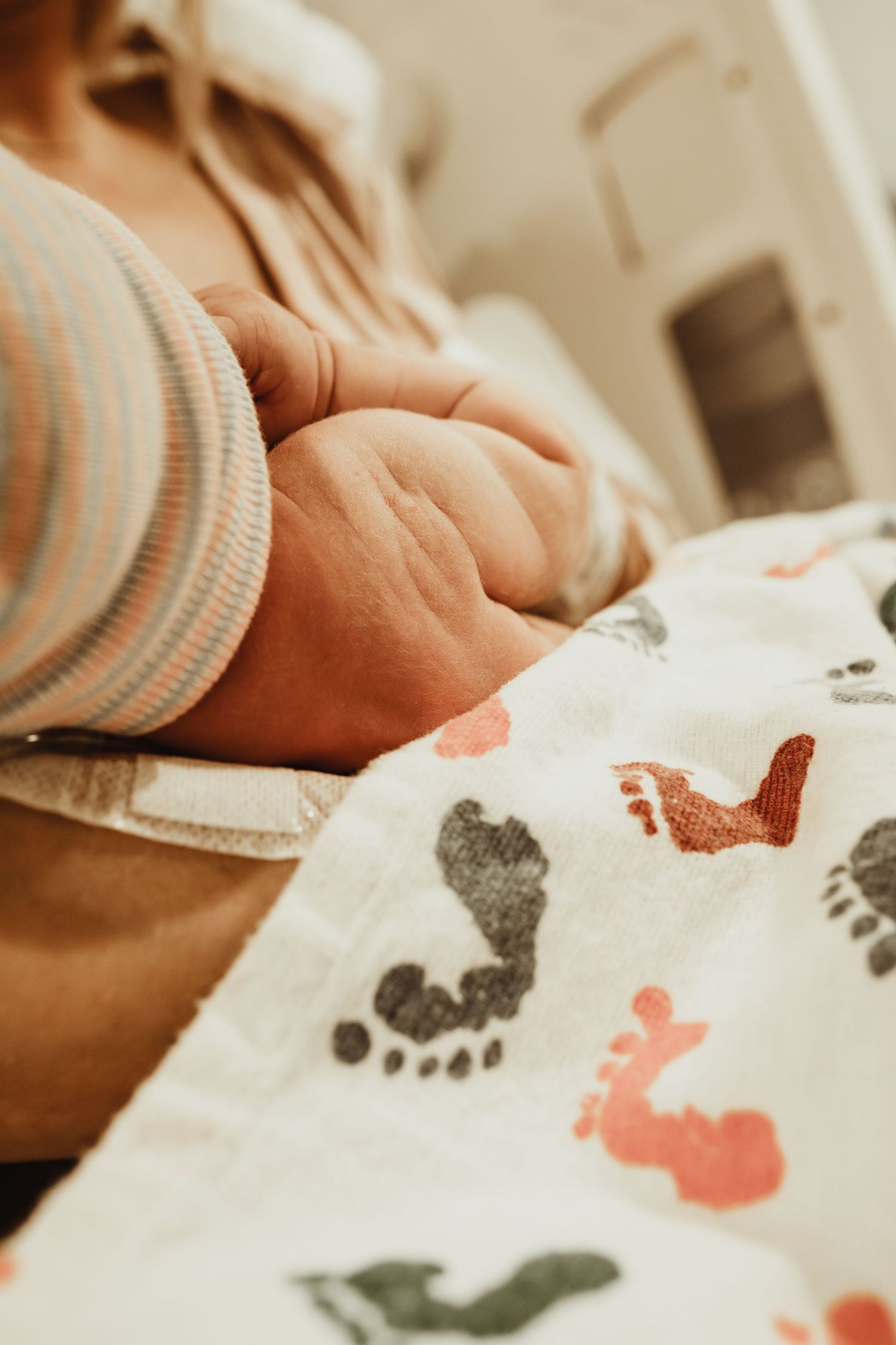 Close-up of baby's hand next to blanket with colorful footprint pattern in coral and gray tones.