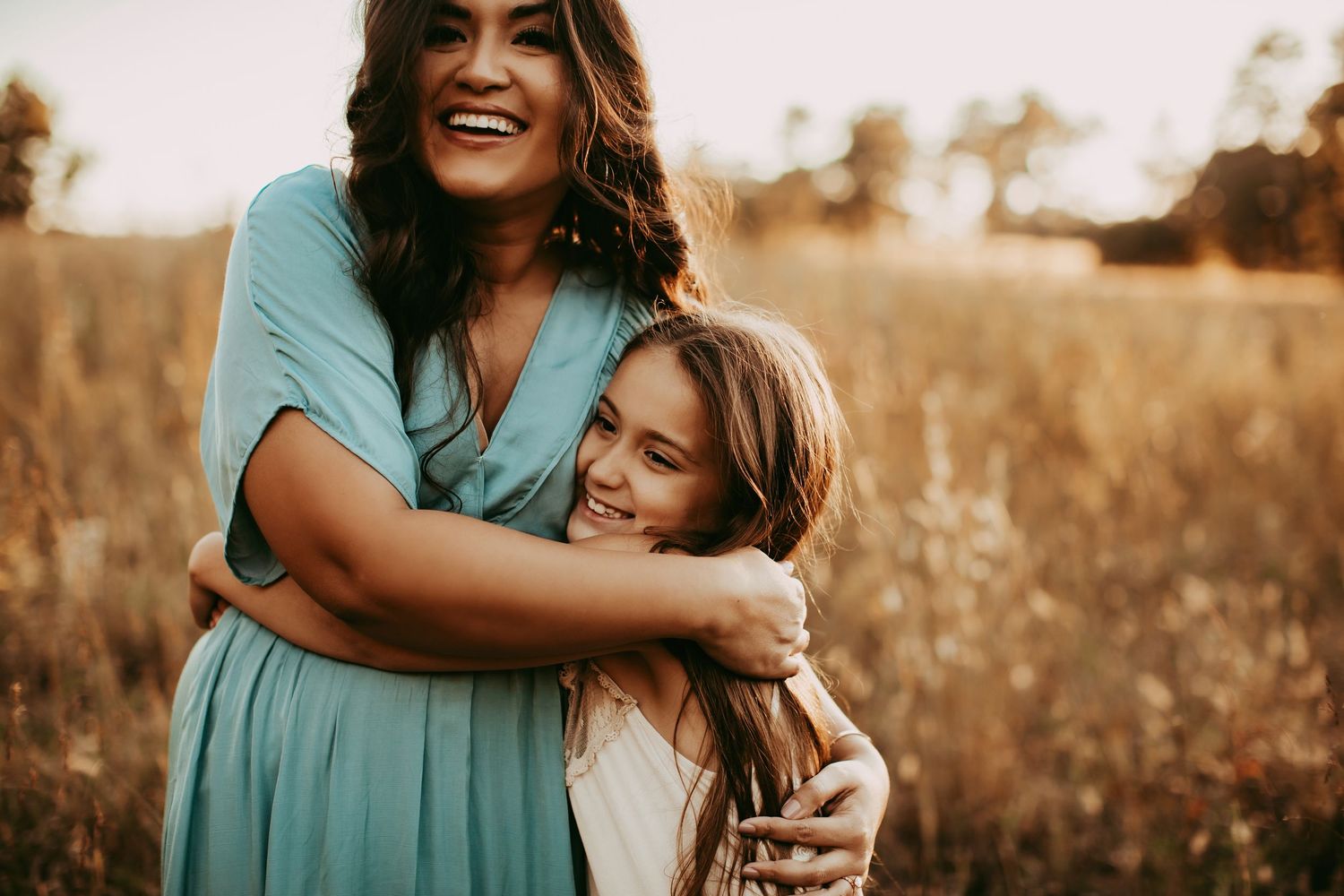 A collection of candid hugging moments captured at sunset in a field with golden light and teal colored outfits.