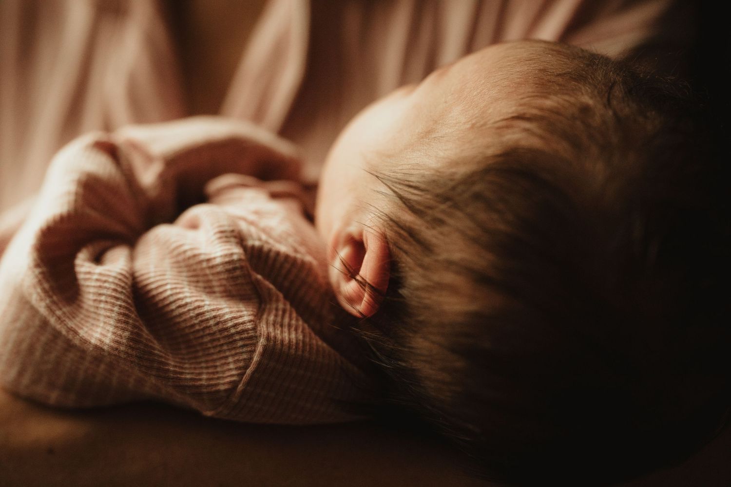 Close-up of a sleeping newborn baby wrapped in a soft pink blanket, cradled in loving arms.