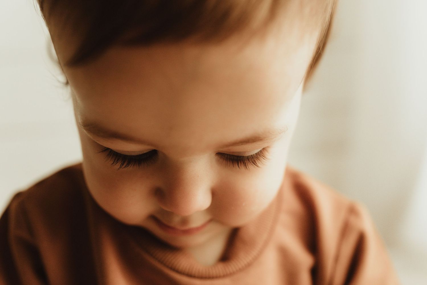 A baby in a white shirt smiles while looking down at something off camera.