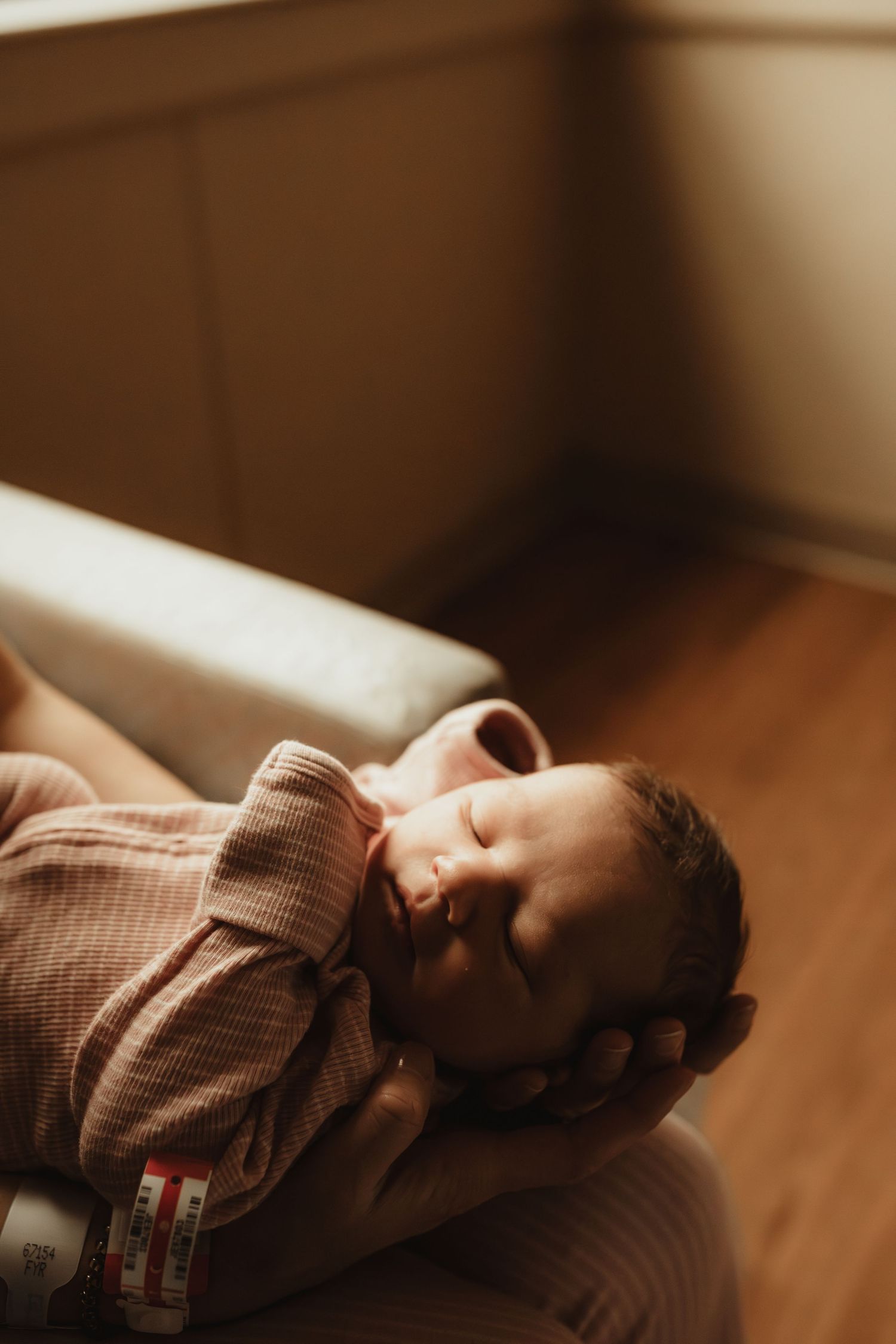 A peaceful newborn baby sleeping in pink onesie cradled in caring hands with warm golden light.