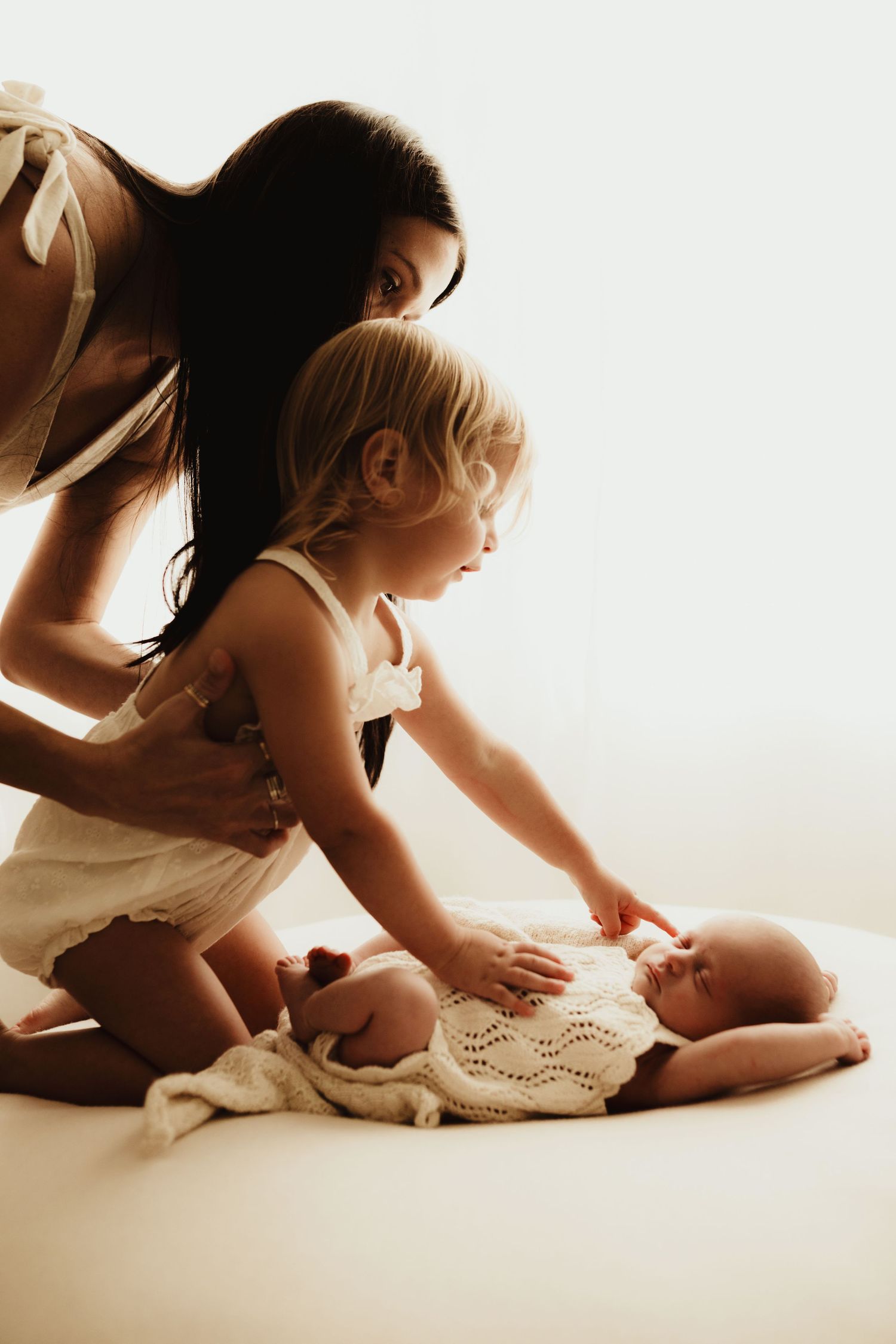 Artistic backlit family portrait session with soft white tones and gentle poses.