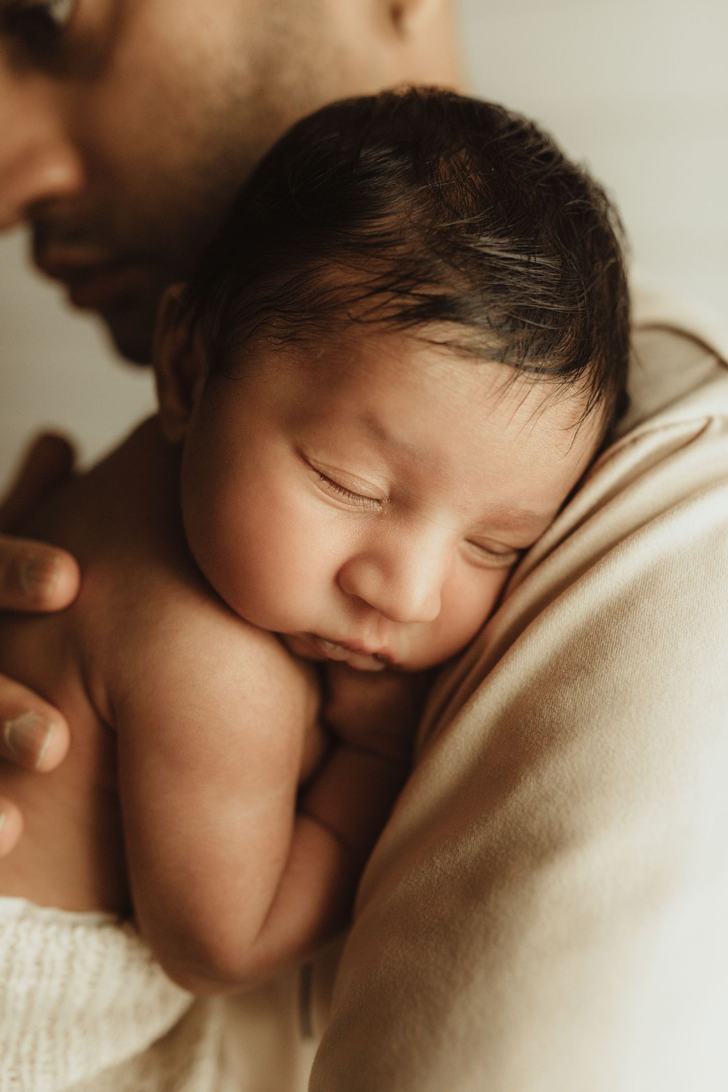 Peaceful sleeping newborn baby resting on someone's shoulder in warm lighting.