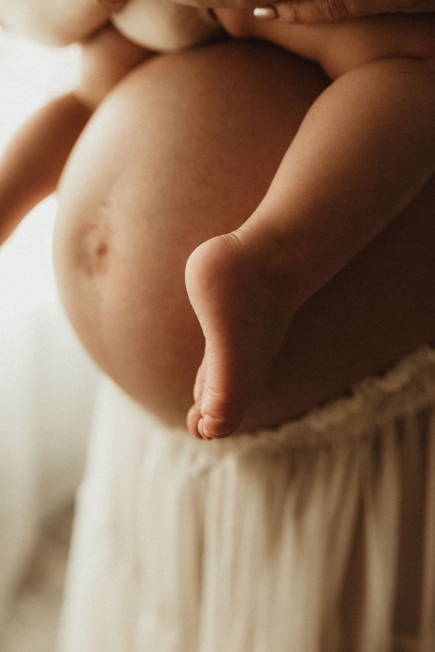 Gentle detail shot of tiny baby toes and feet against mother's pregnant belly.