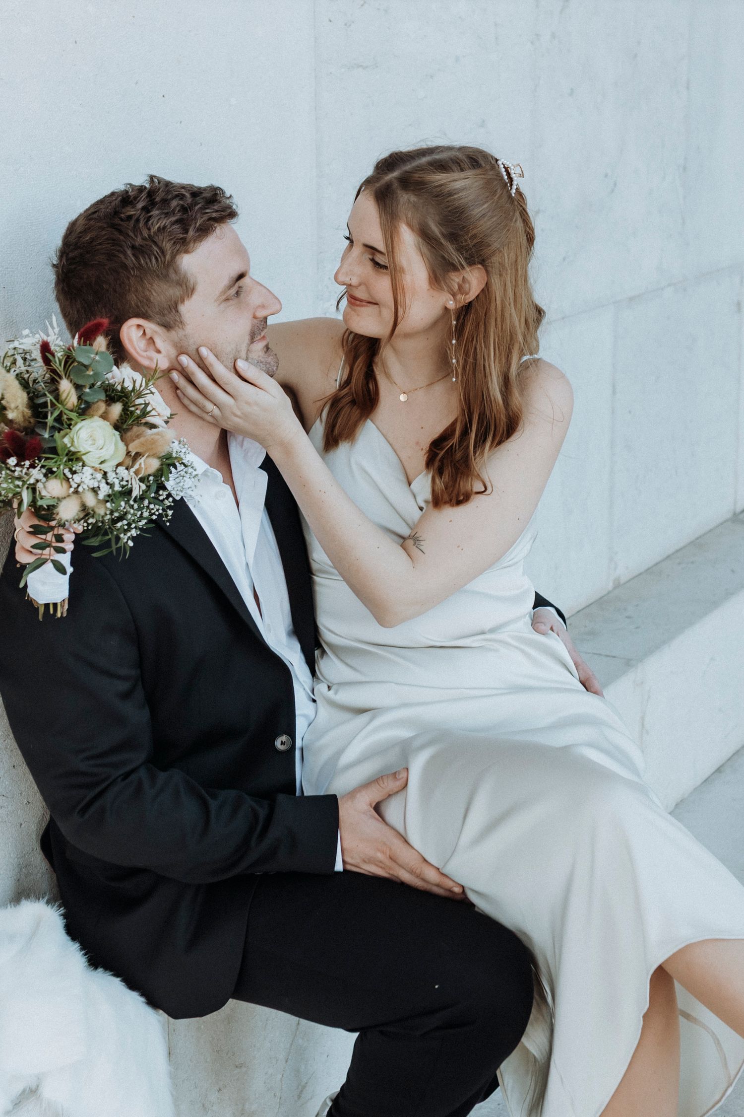 Elegant couple in formal wear sharing intimate moments against a light background.