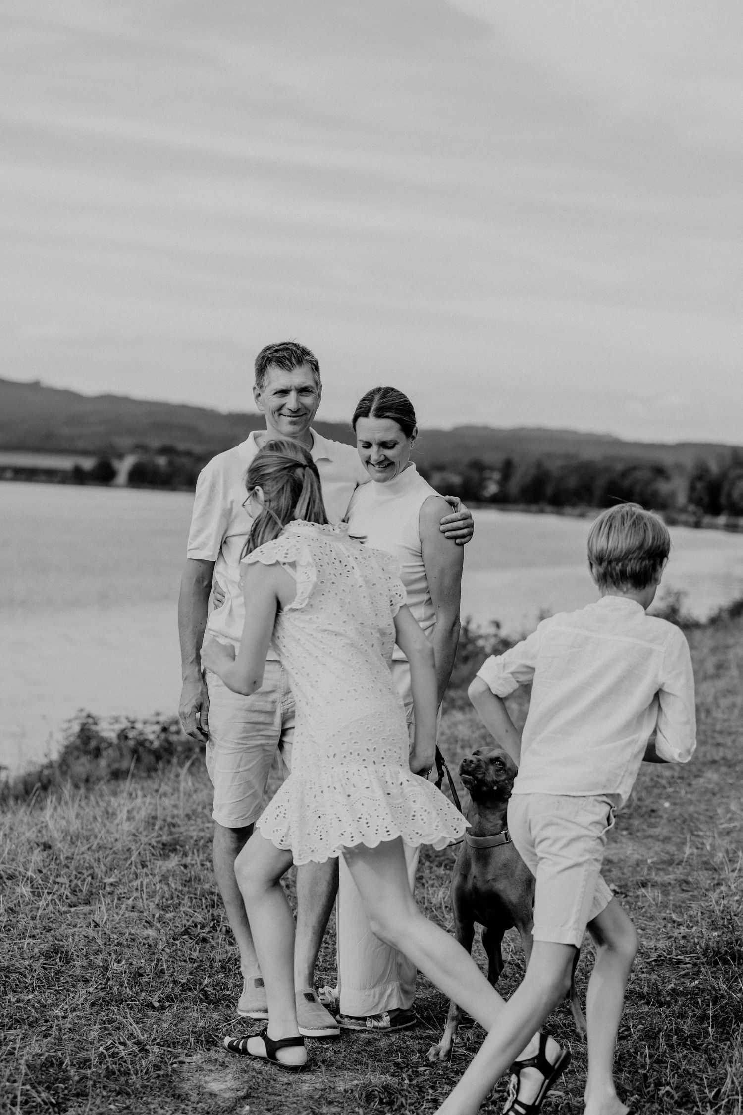 Family and dog enjoying a casual moment together on a grassy hillside.