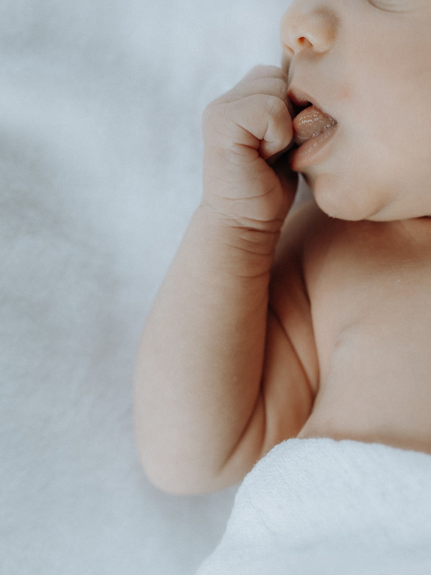 Close-up of a baby's mouth and hand in soft, dreamy lighting.