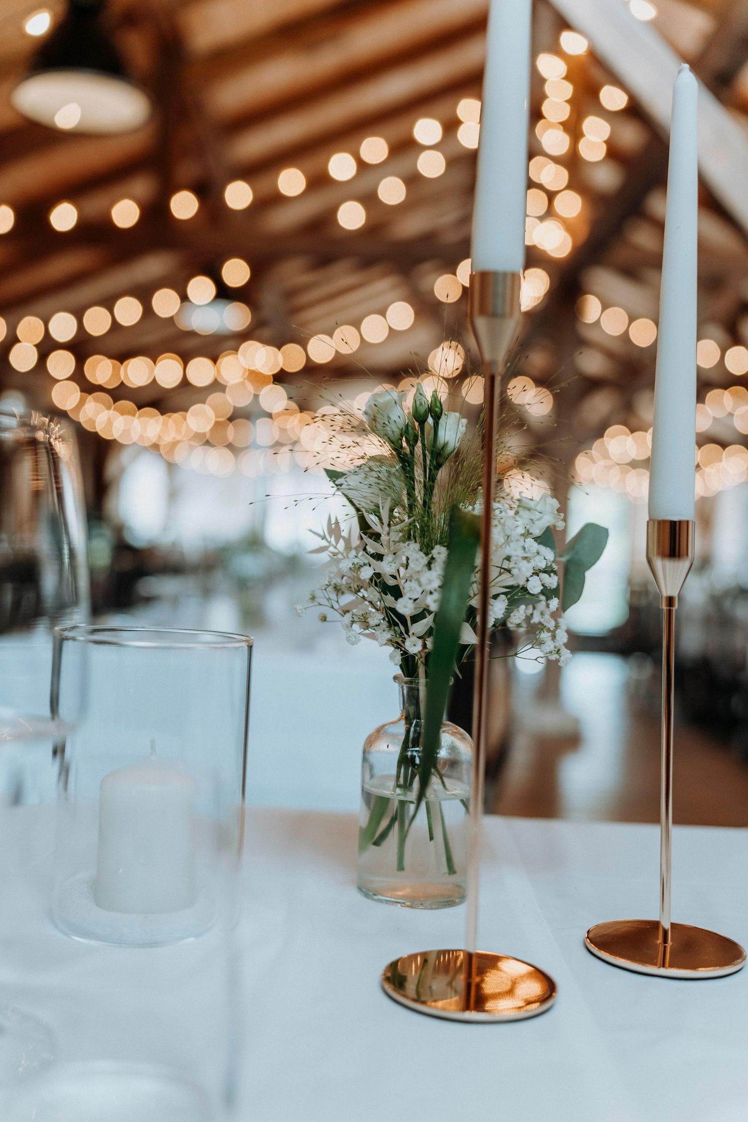 Elegant wedding reception table setting with candlesticks and delicate flowers under string lights.