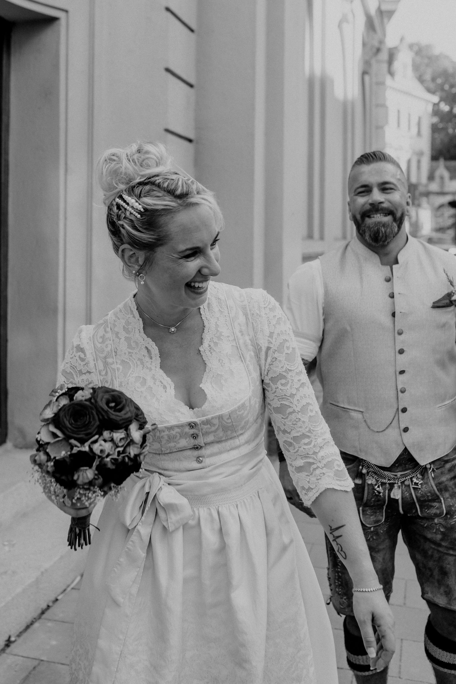 Traditional Bavarian wedding couple laughing together outside a historic building.