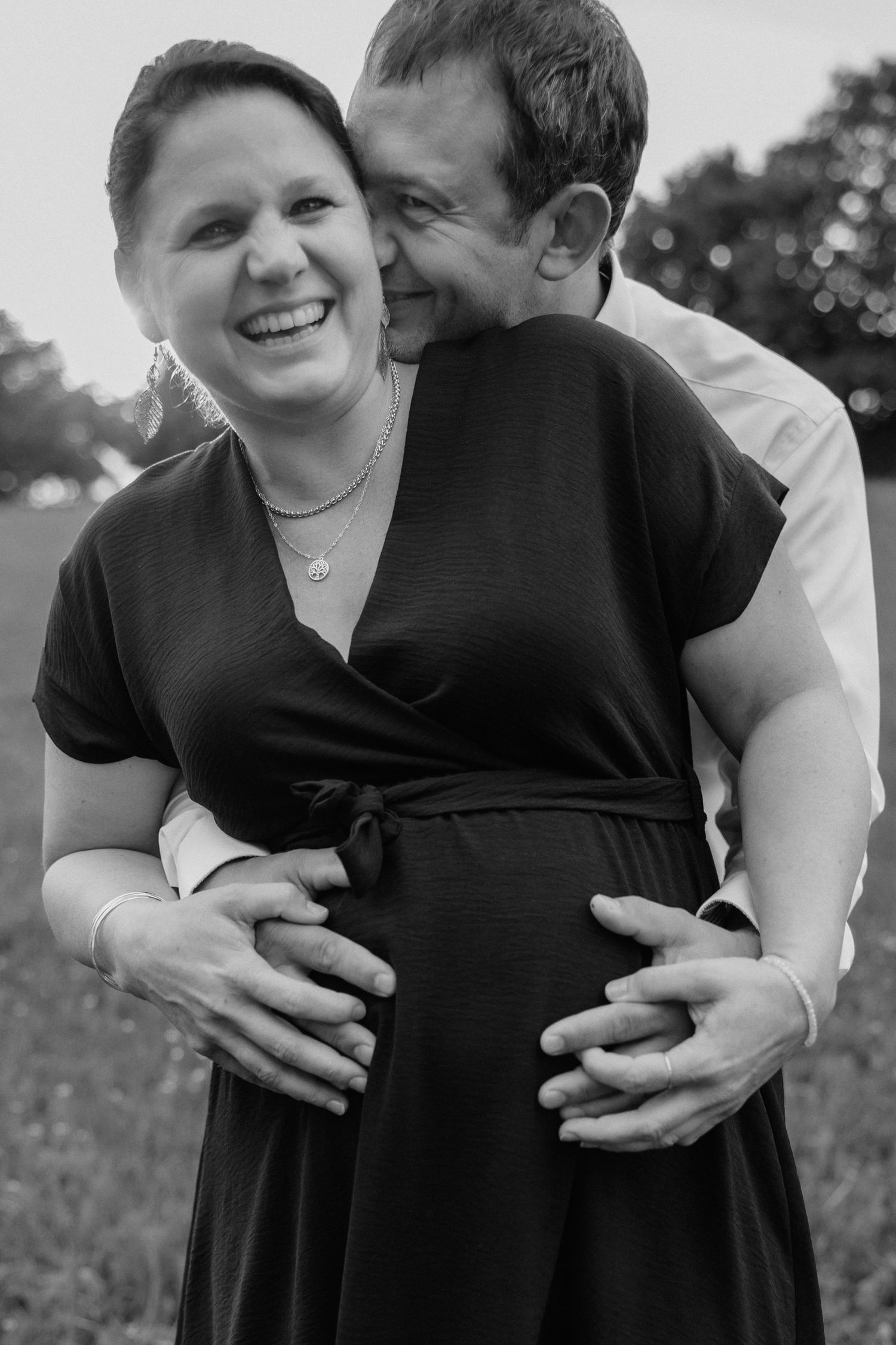 Black and white portrait of joyful expecting couple embracing outdoors.