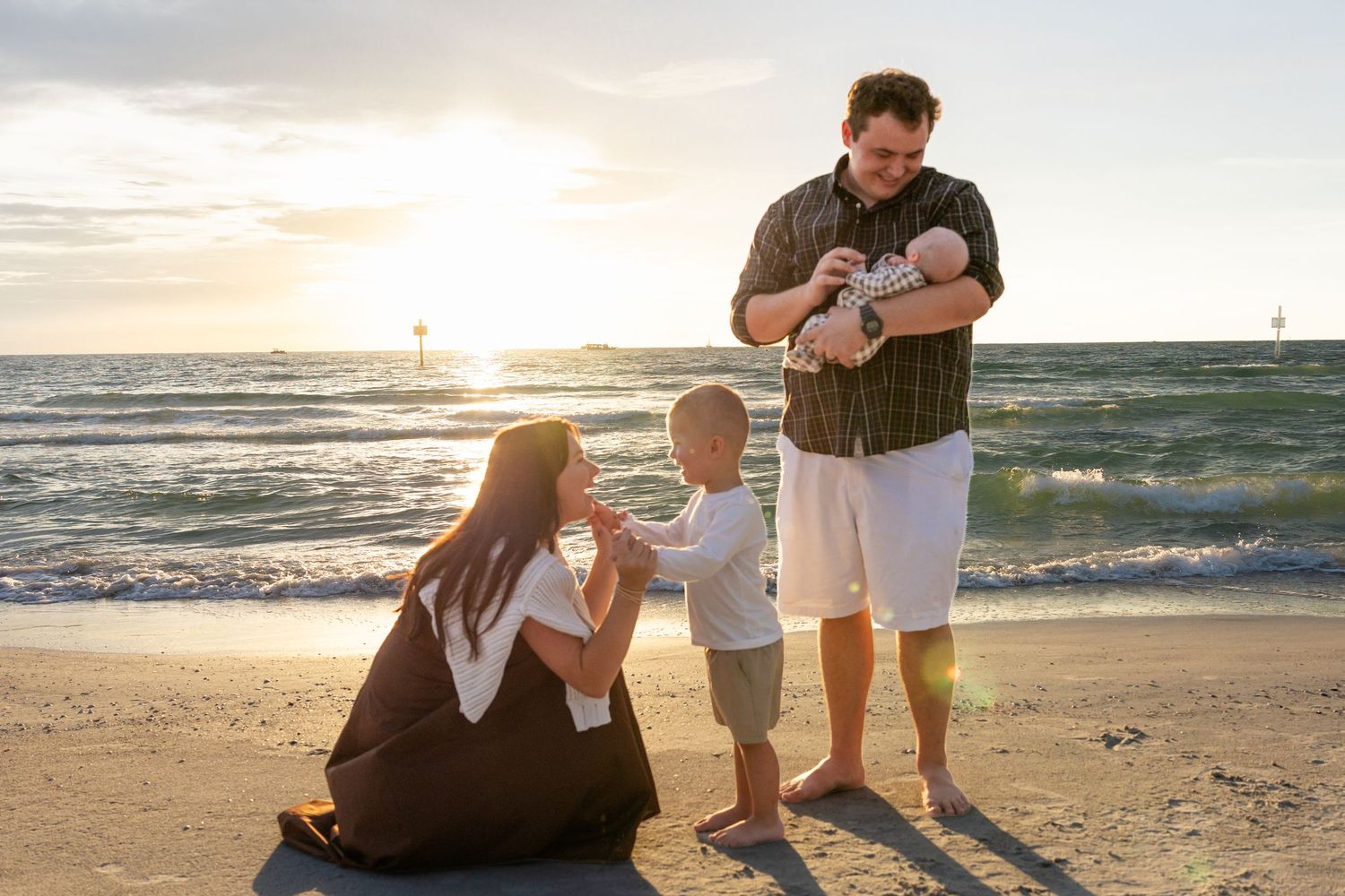 Young family with toddler and newborn baby enjoying a beautiful sunset on the beach.
