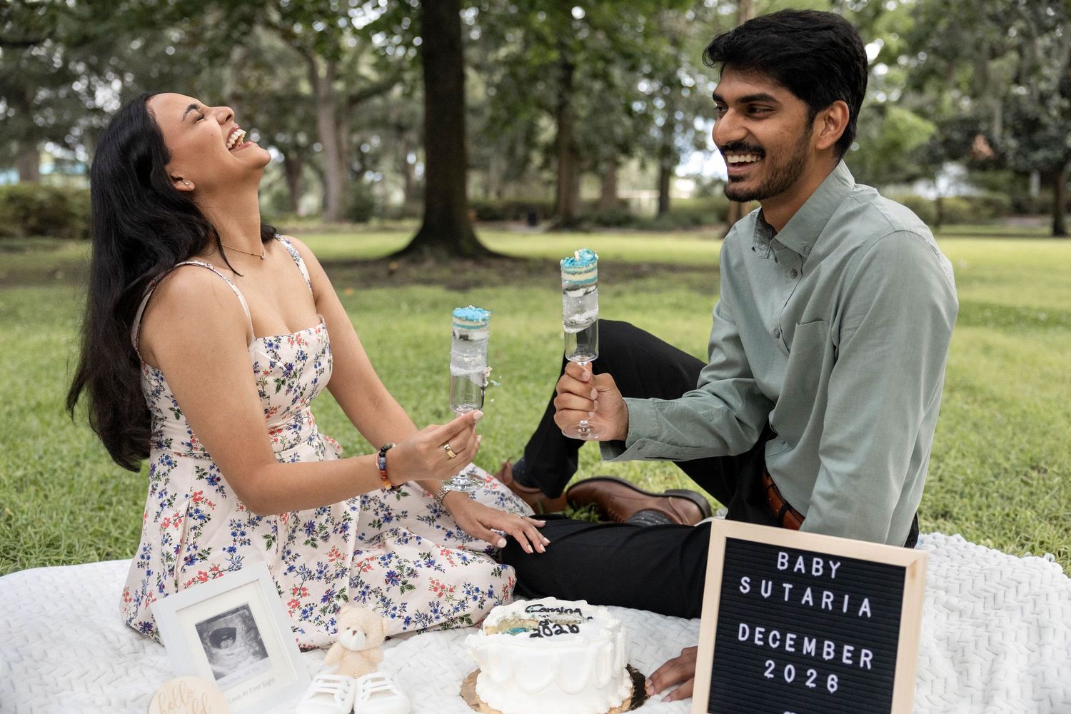 Couple celebrating pregnancy announcement with cake beside a Baby Sutaria December 2026 sign.