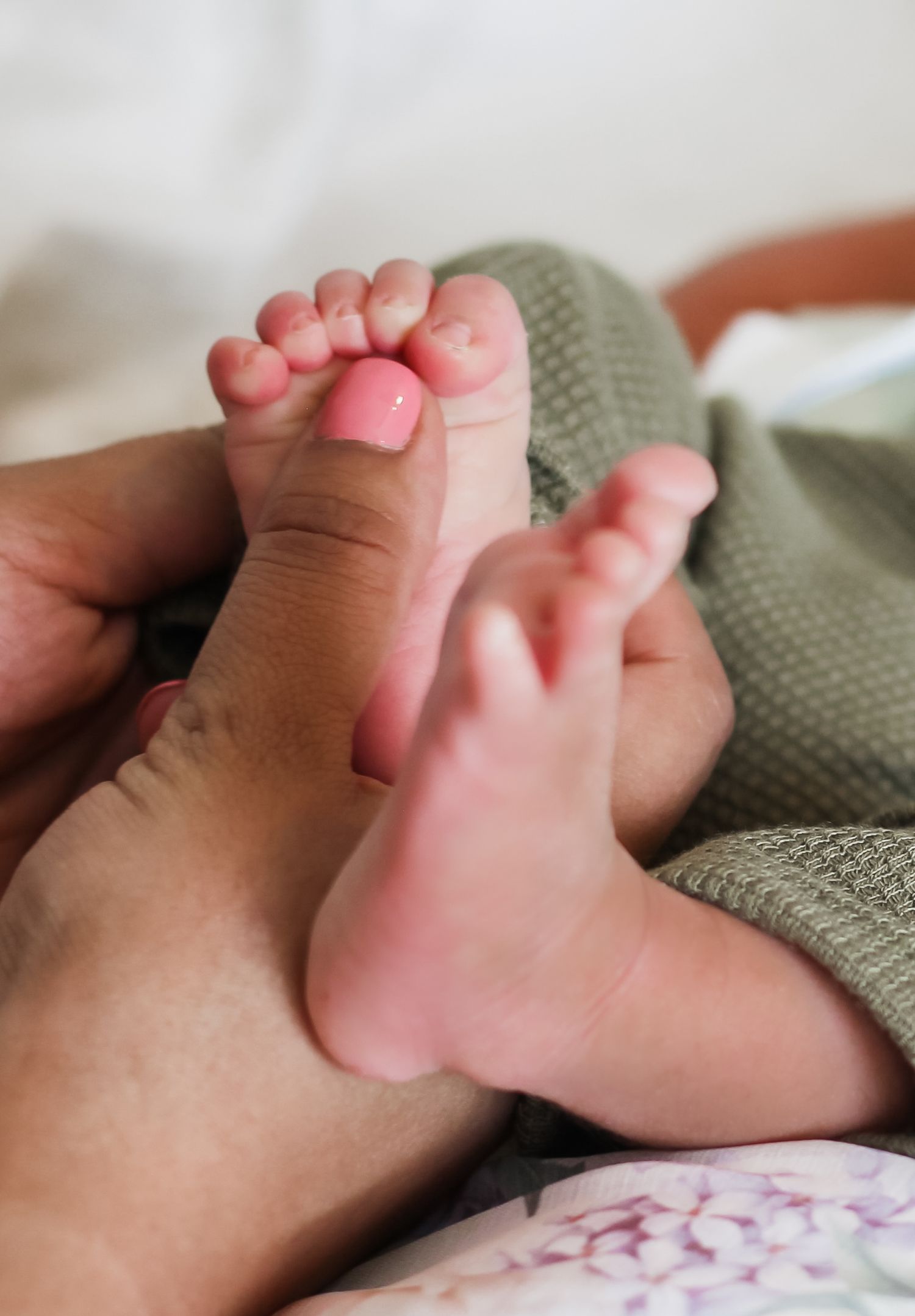 Close-up of newborn baby tiny feet cradled gently in parent hands on soft bedding.