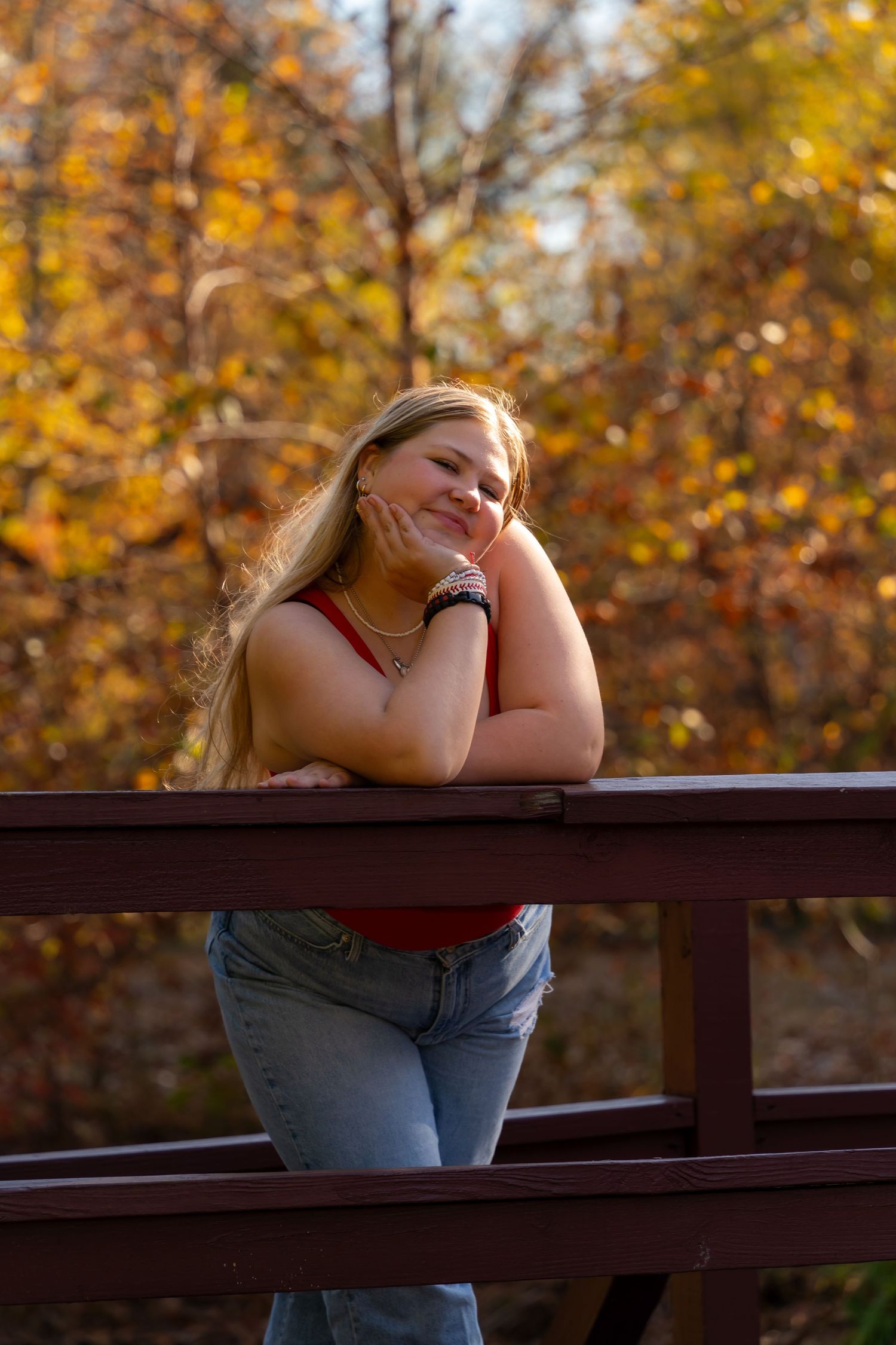 Autumn portrait leaning on wooden railing with colorful fall foliage in background.