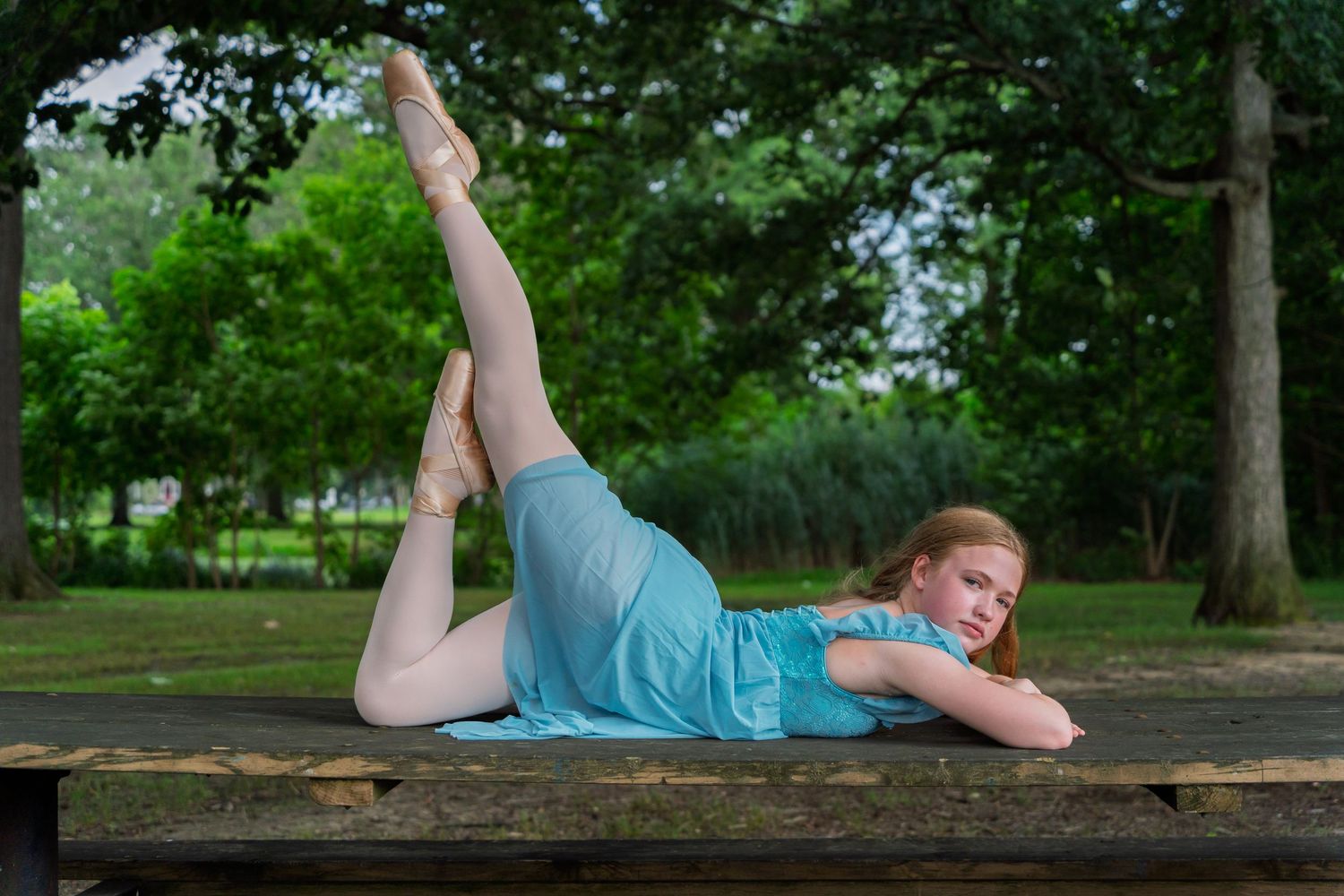 A person in a turquoise shirt lies on a fallen tree trunk in a lush green park setting.