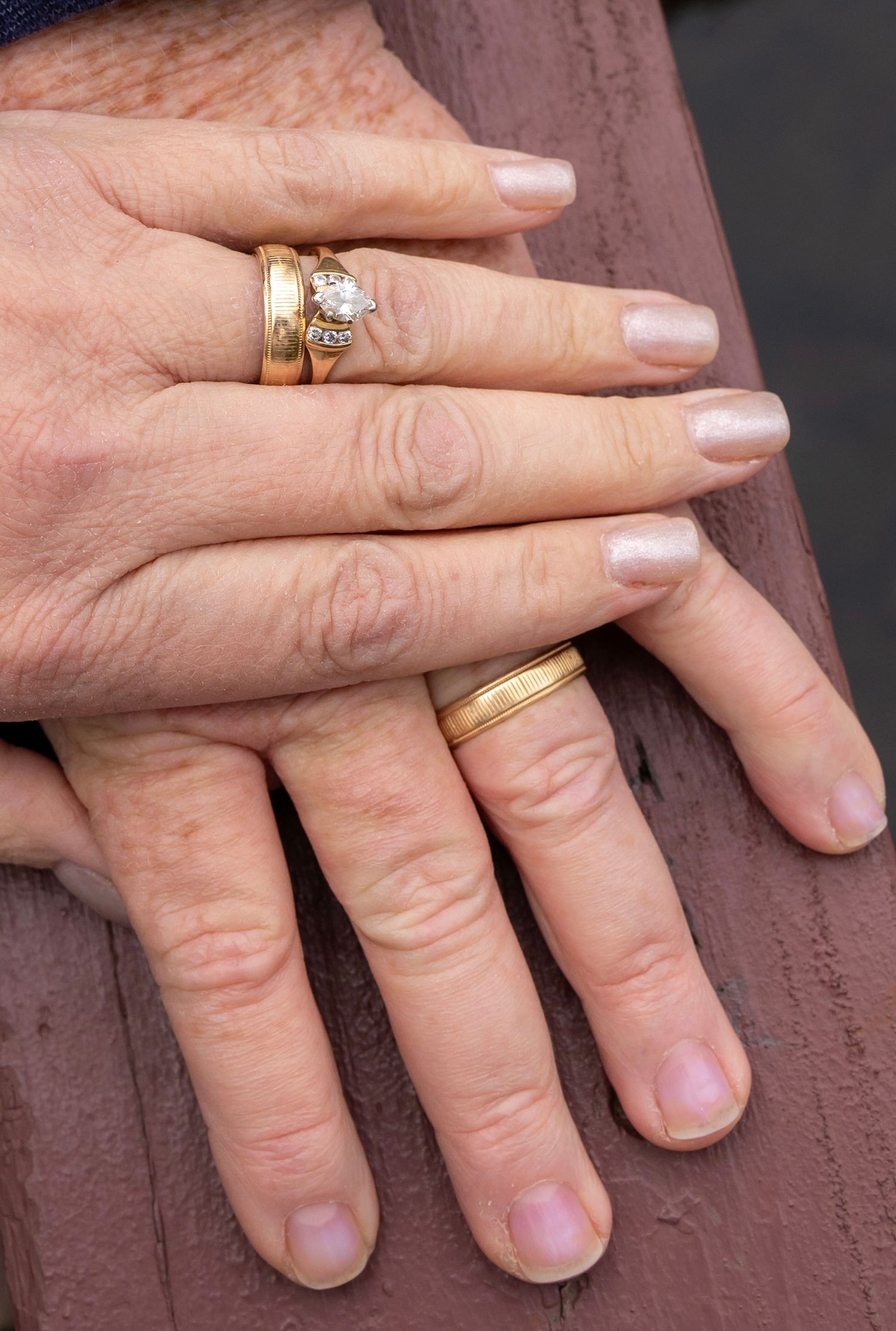 Close-up of hands displaying wedding rings against wooden railing background.