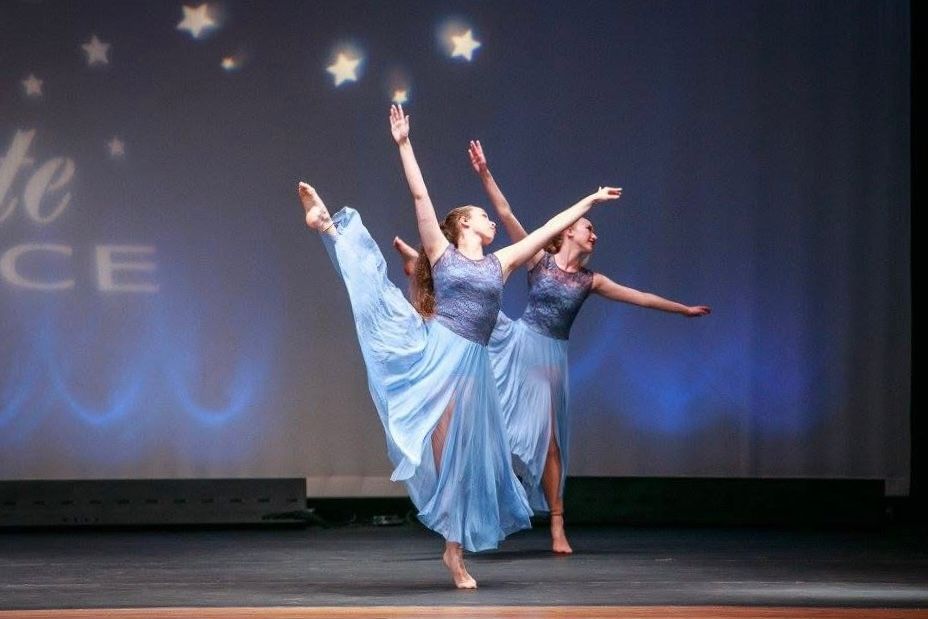 Dancers in light blue costumes perform elegant movements on a darkened stage.