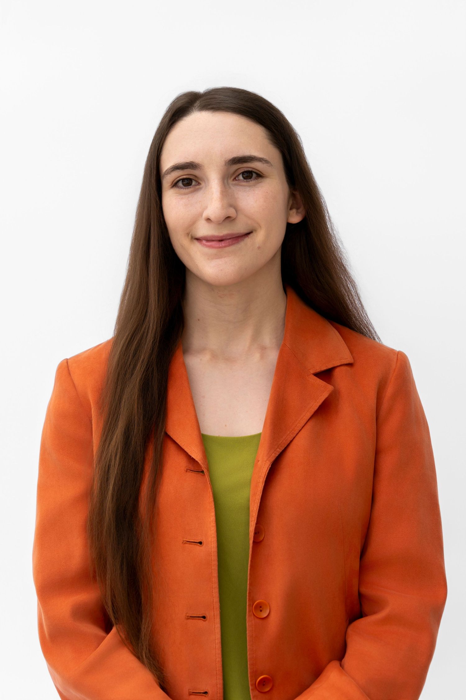 Professional portrait of someone wearing a bright orange blazer and lime green top against a white background.