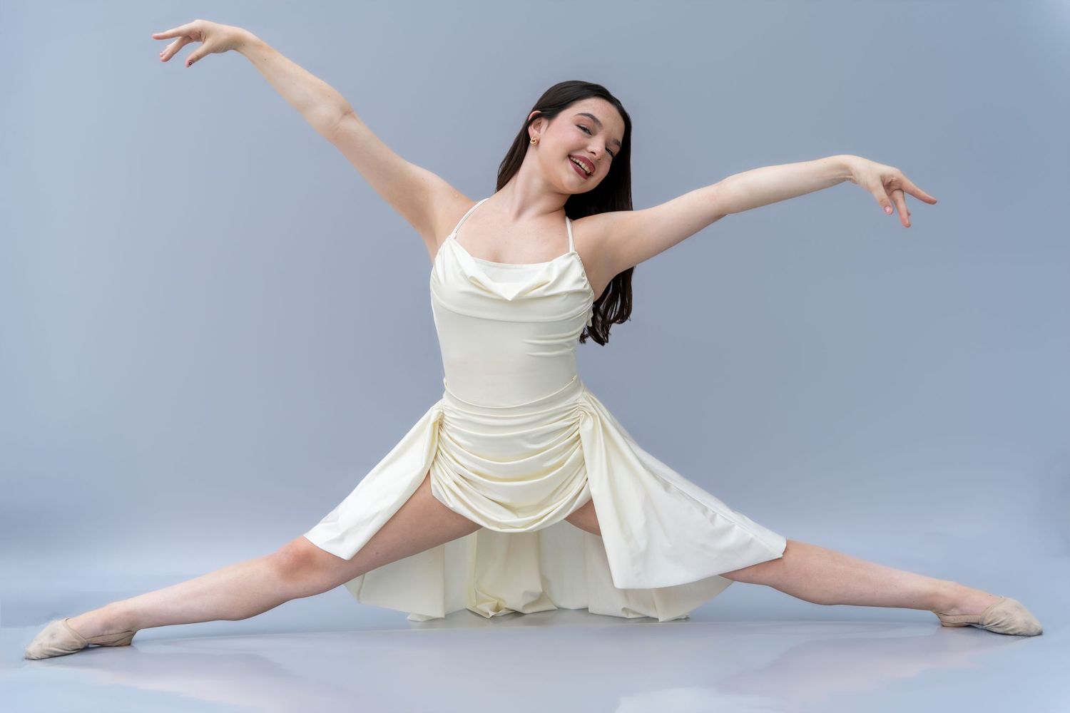 A graceful dancer in a cream-colored dress performs a series of elegant leaping and stretching movements against a blue backdrop.