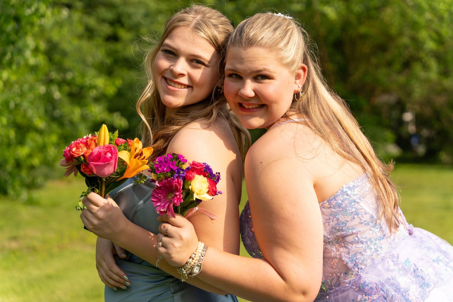 Two people in formal dresses holding colorful bouquets outdoors.