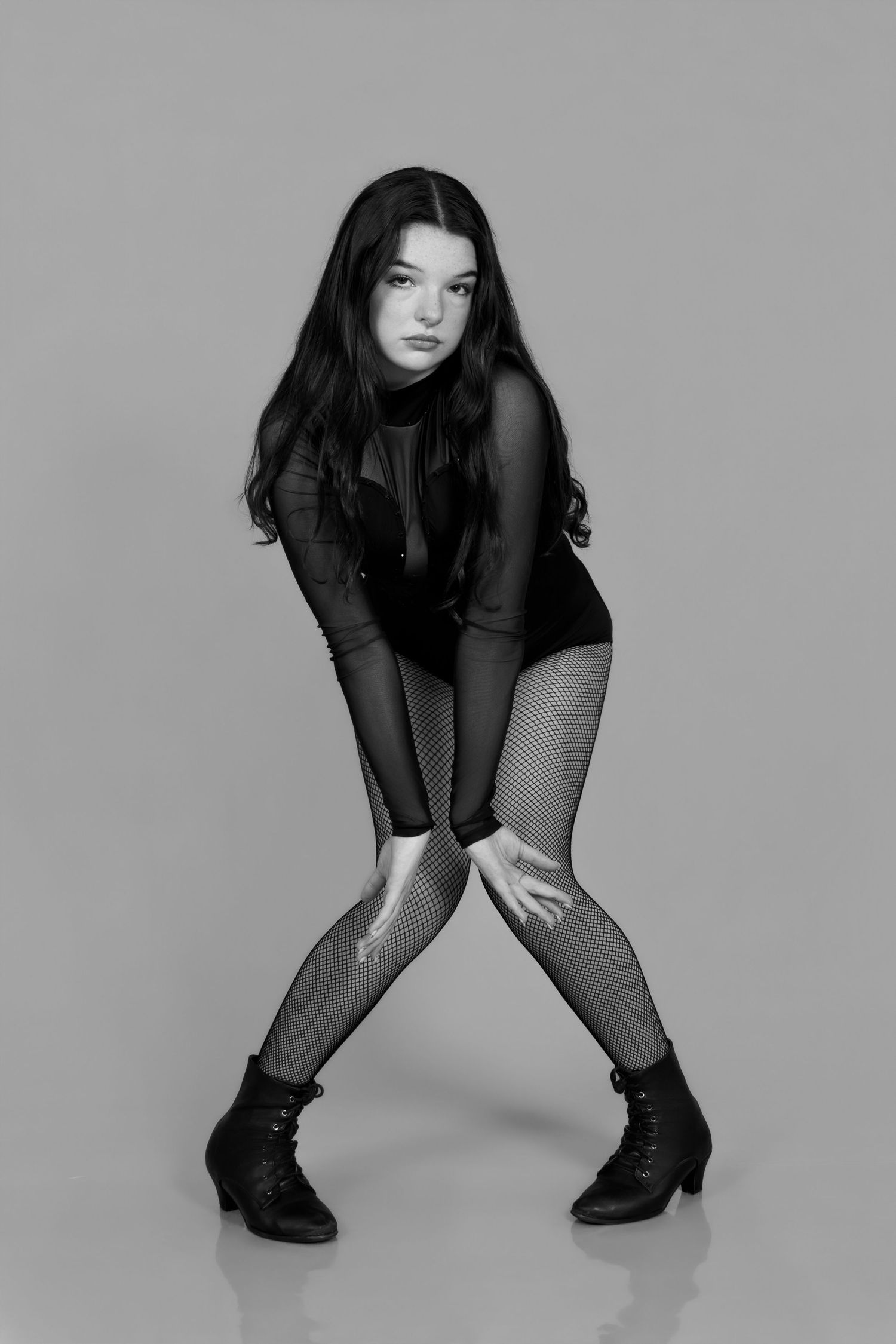 Black and white photo of a young woman in fishnet leggings and ankle boots striking a dance pose.