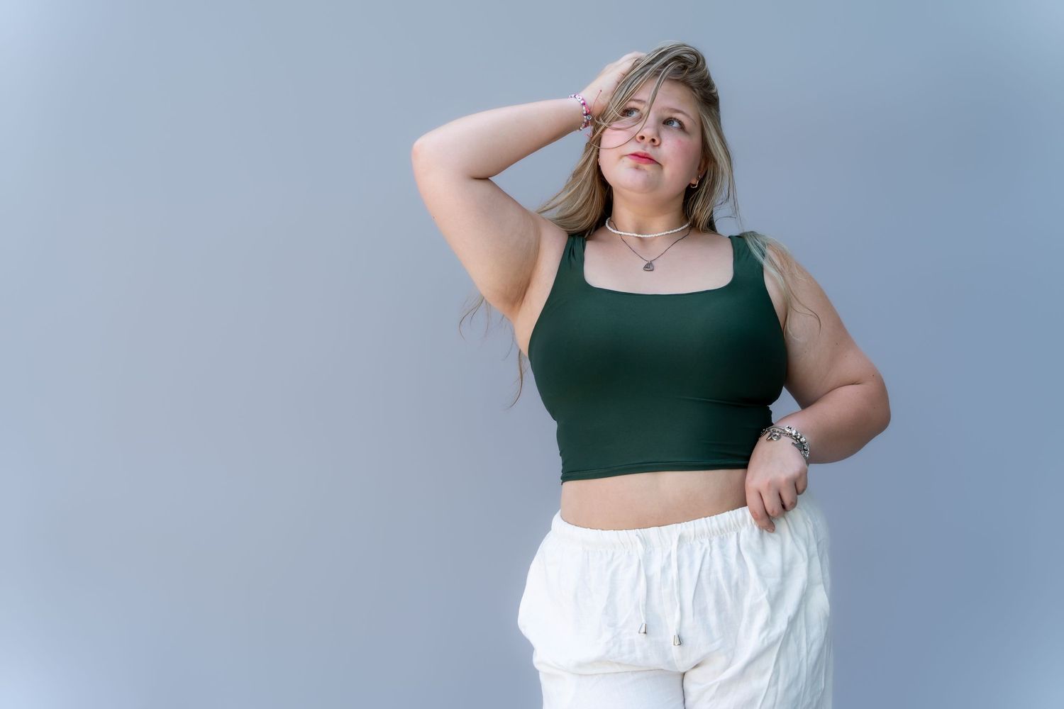 Person in dark green crop top and white pants poses against light background in fashion photoshoot series.