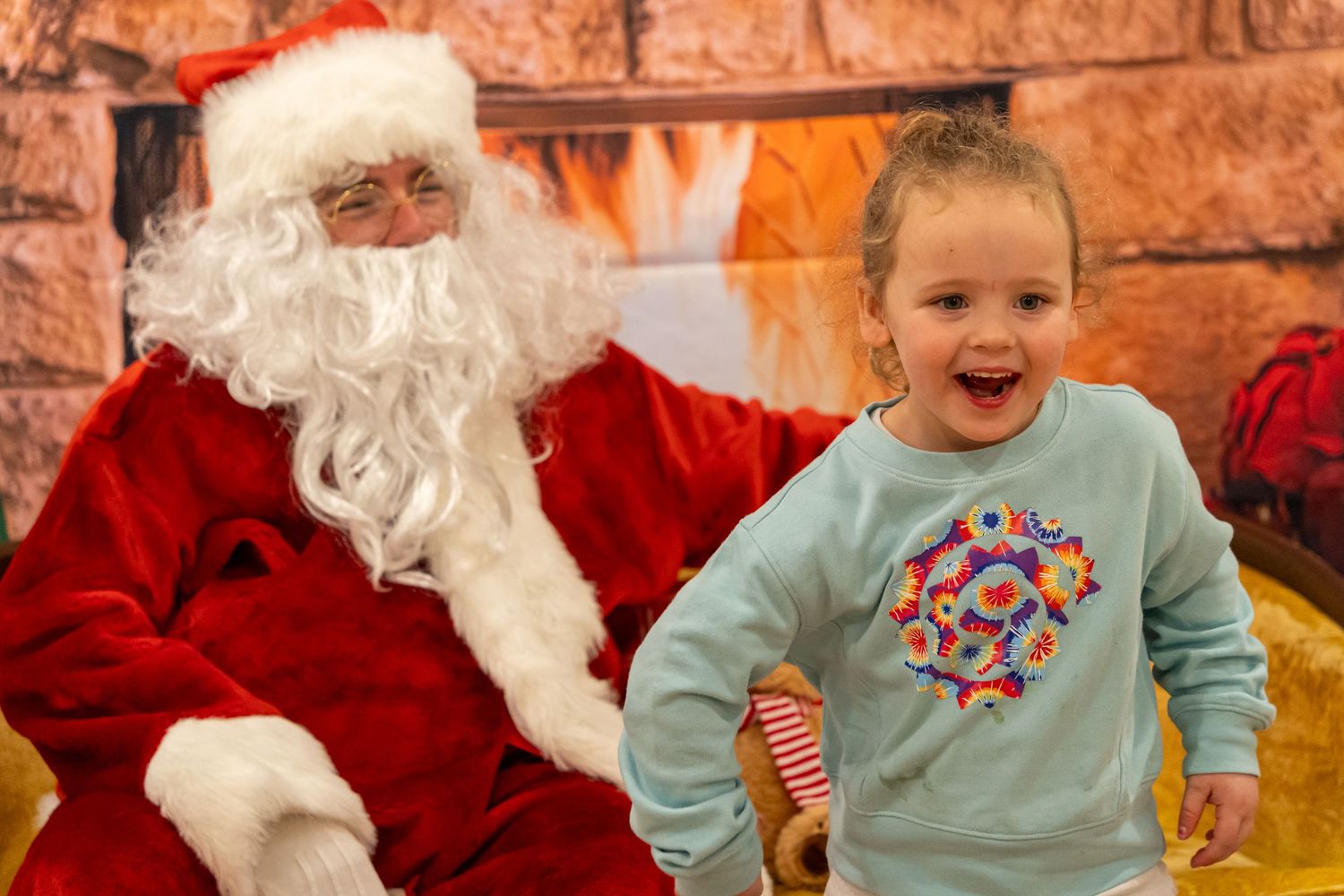 A joyful holiday moment captured with Santa and a delighted visitor in a blue sweater.